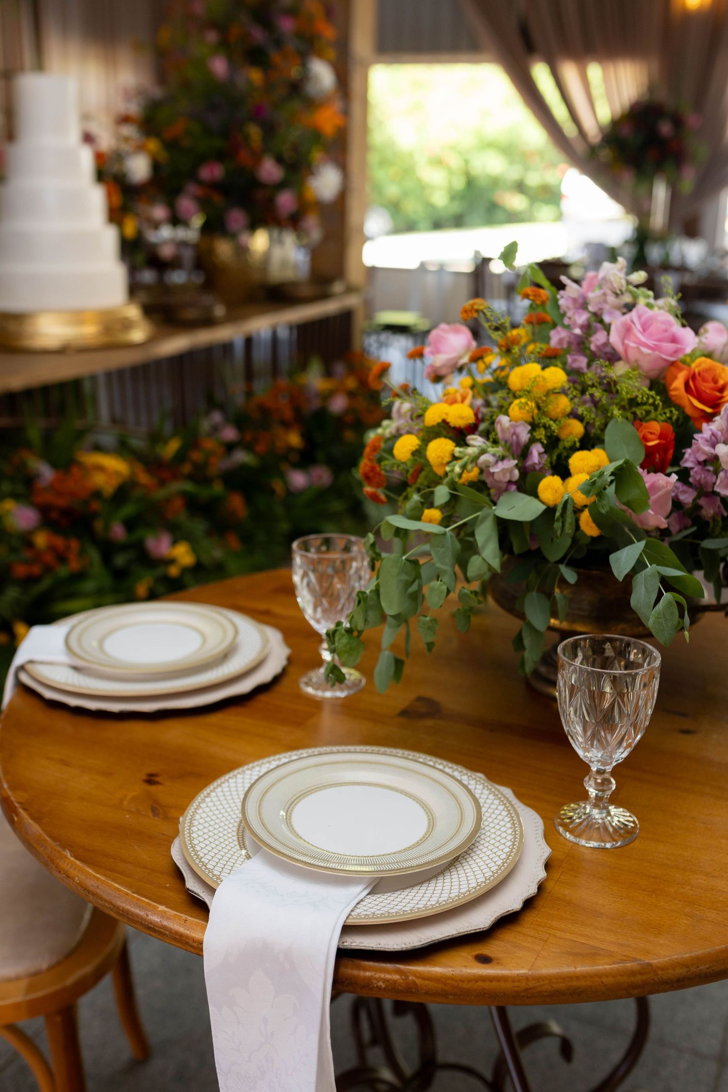 Elegant wedding table setting with gold-rimmed plates, crystal glasses, and a vibrant floral centerpiece on a wooden round table.