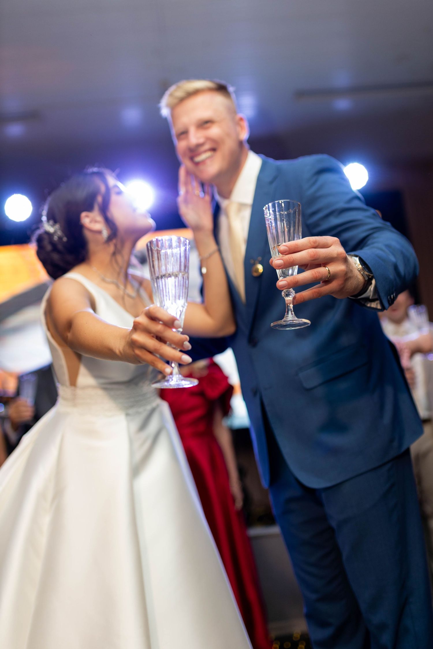 Bride and groom toasting with champagne glasses at wedding reception, groom in blue suit smiling.