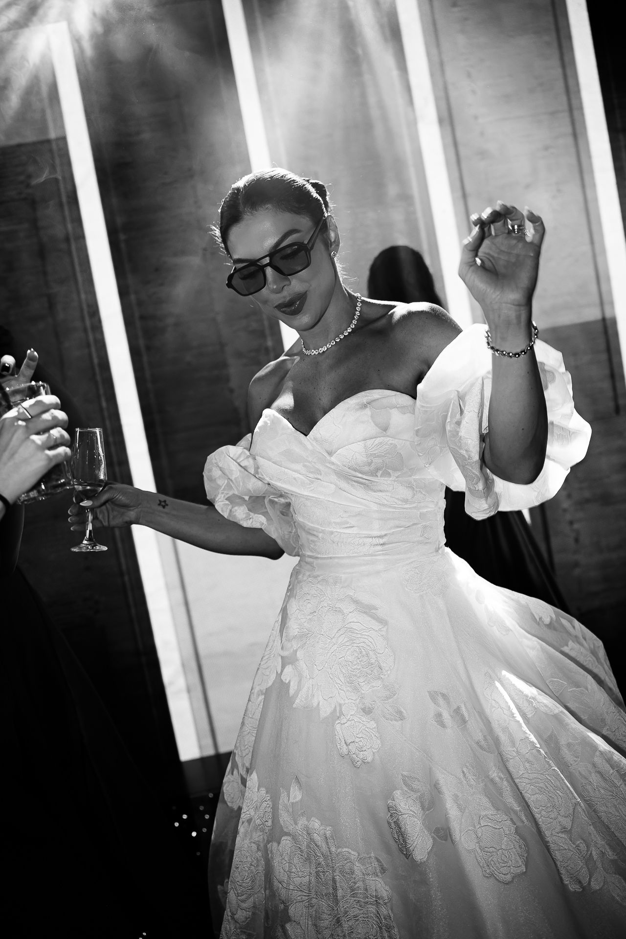 Black and white photo of a bride in a strapless gown and sunglasses dancing joyfully at her wedding reception.