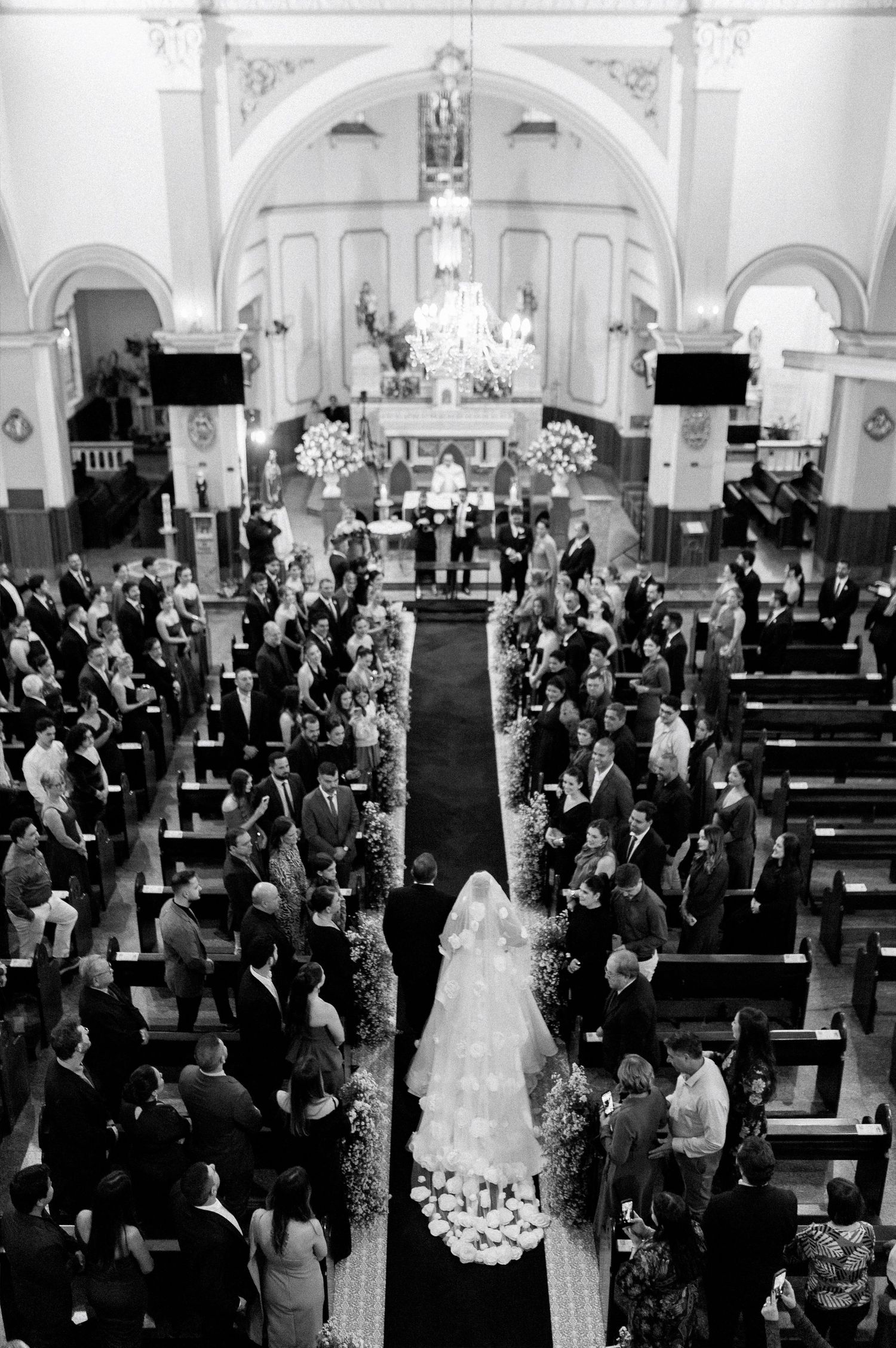Aerial view of a bride walking down the aisle in a crowded church during a wedding ceremony.