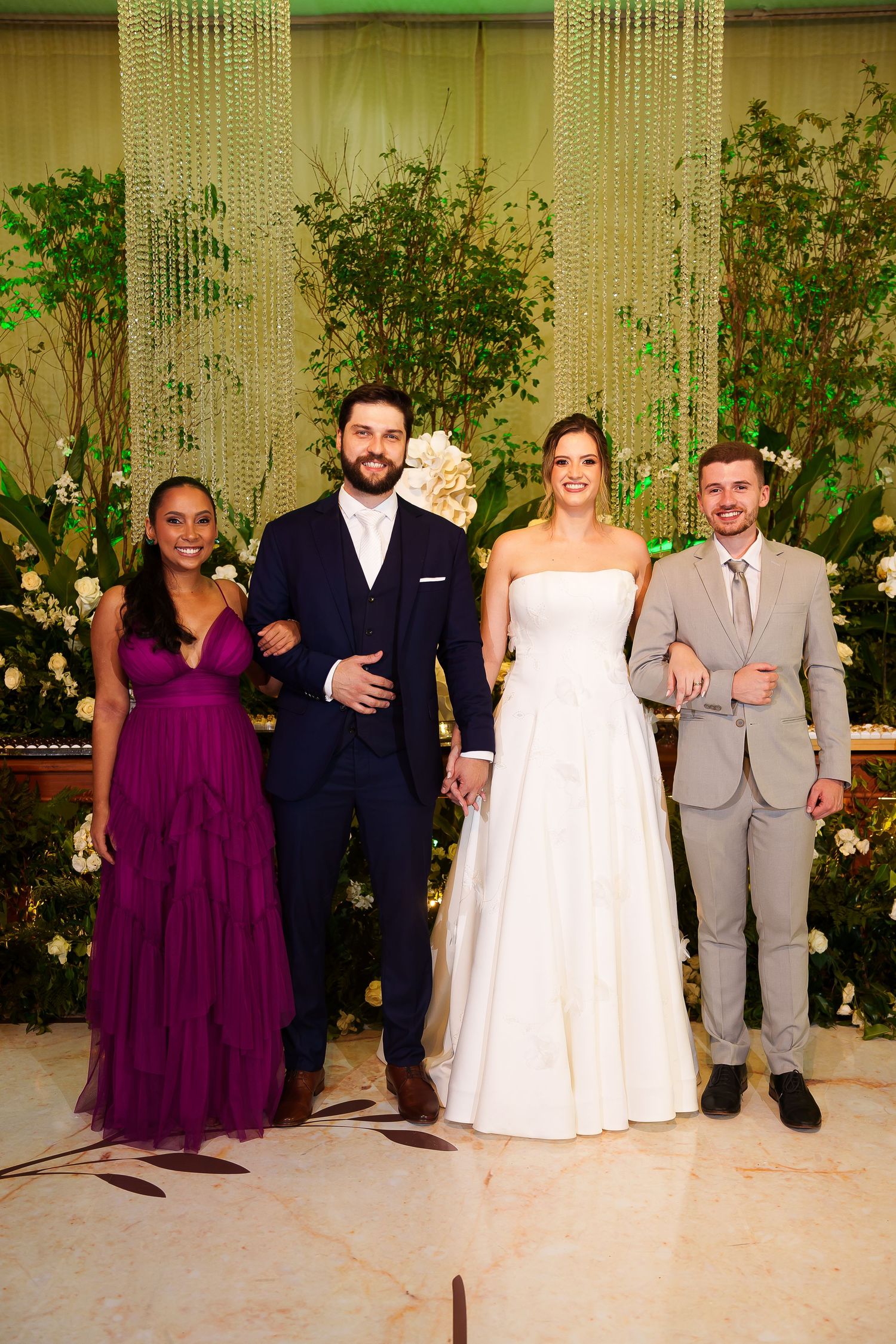 Wedding party posing elegantly, bride in white gown, groom in navy suit, guests in purple dress and gray suit.