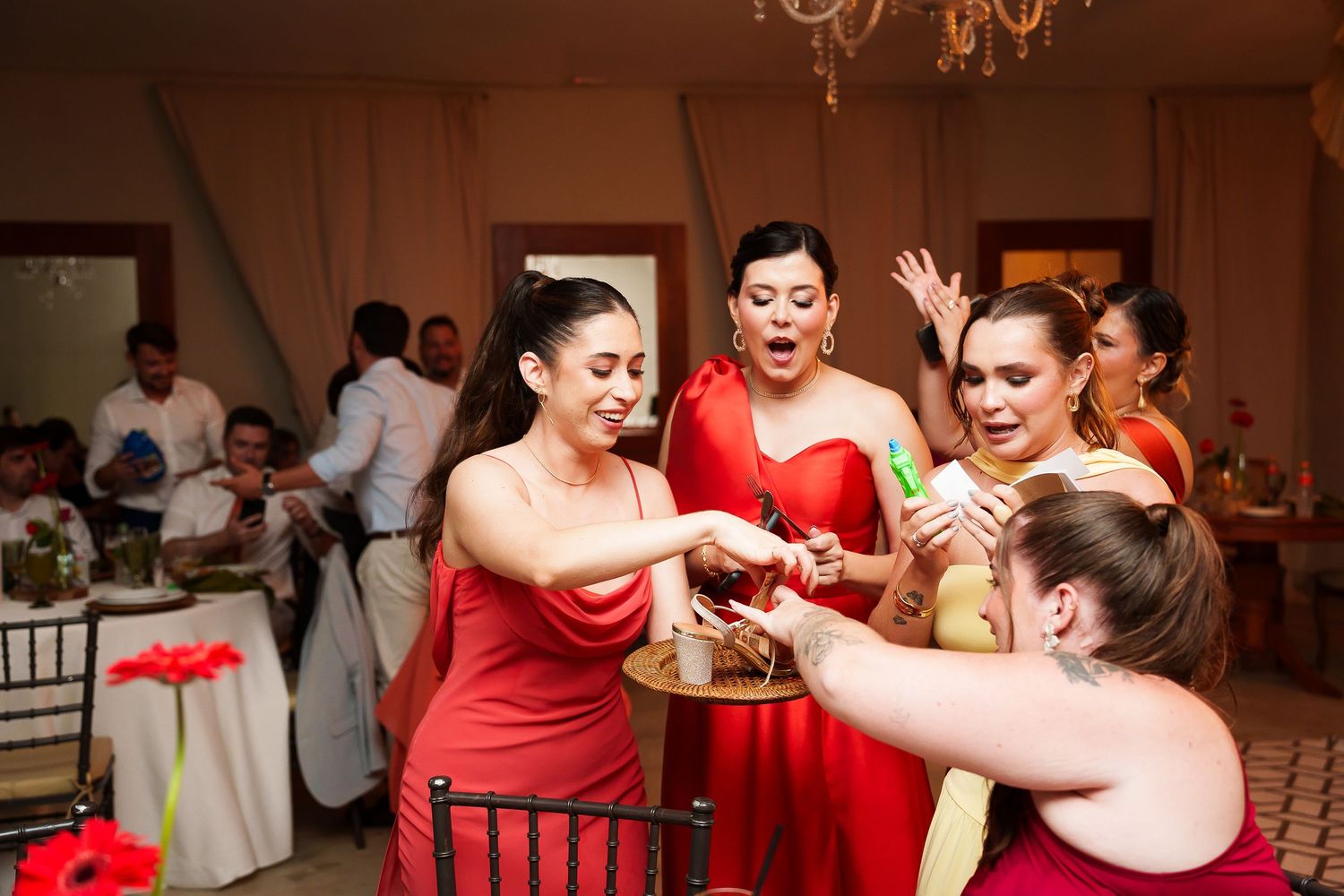 Bridesmaids in red dresses celebrate at a wedding reception, pouring drinks and laughing together.