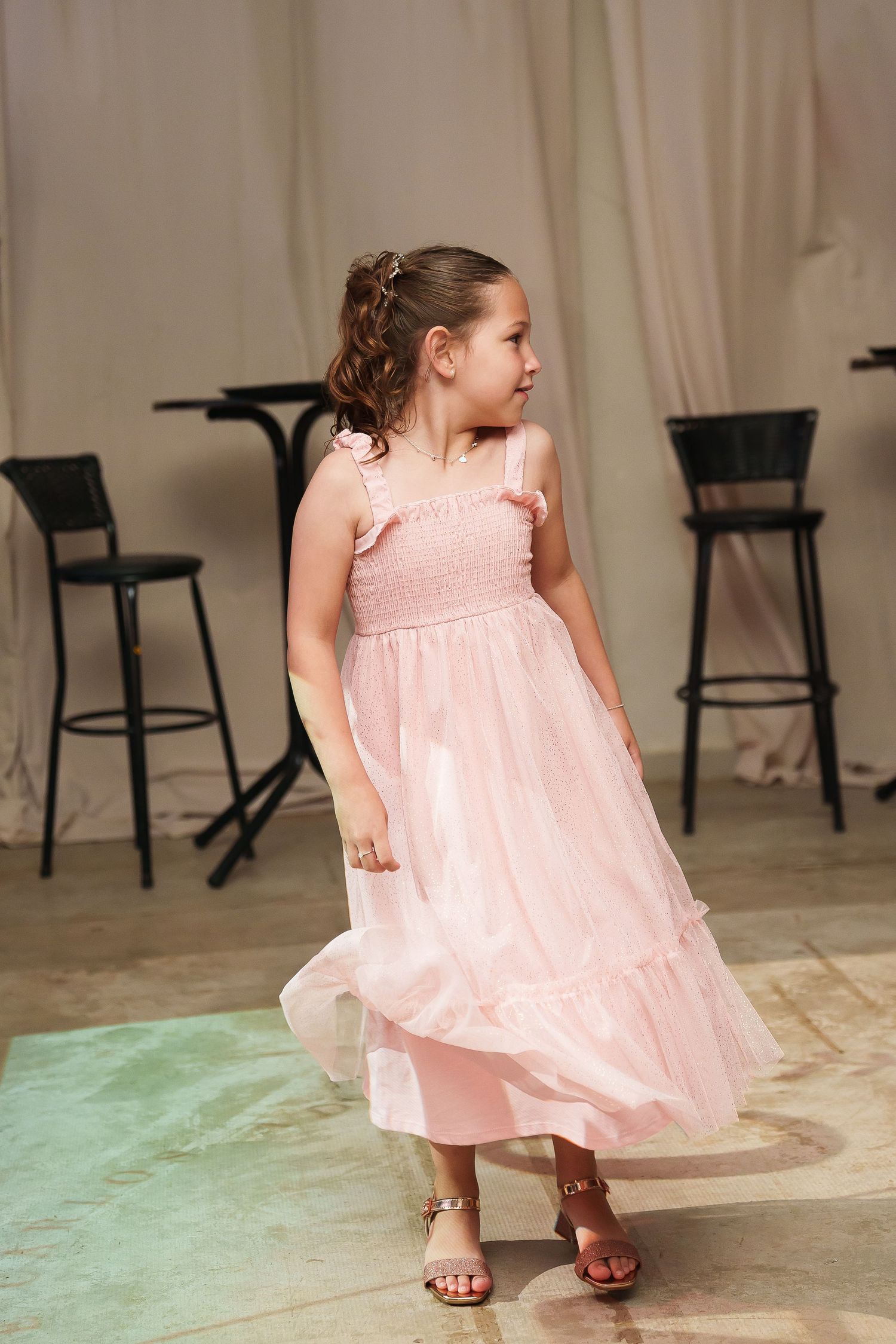 Young girl twirling in a pink dress on a dance floor at an event.