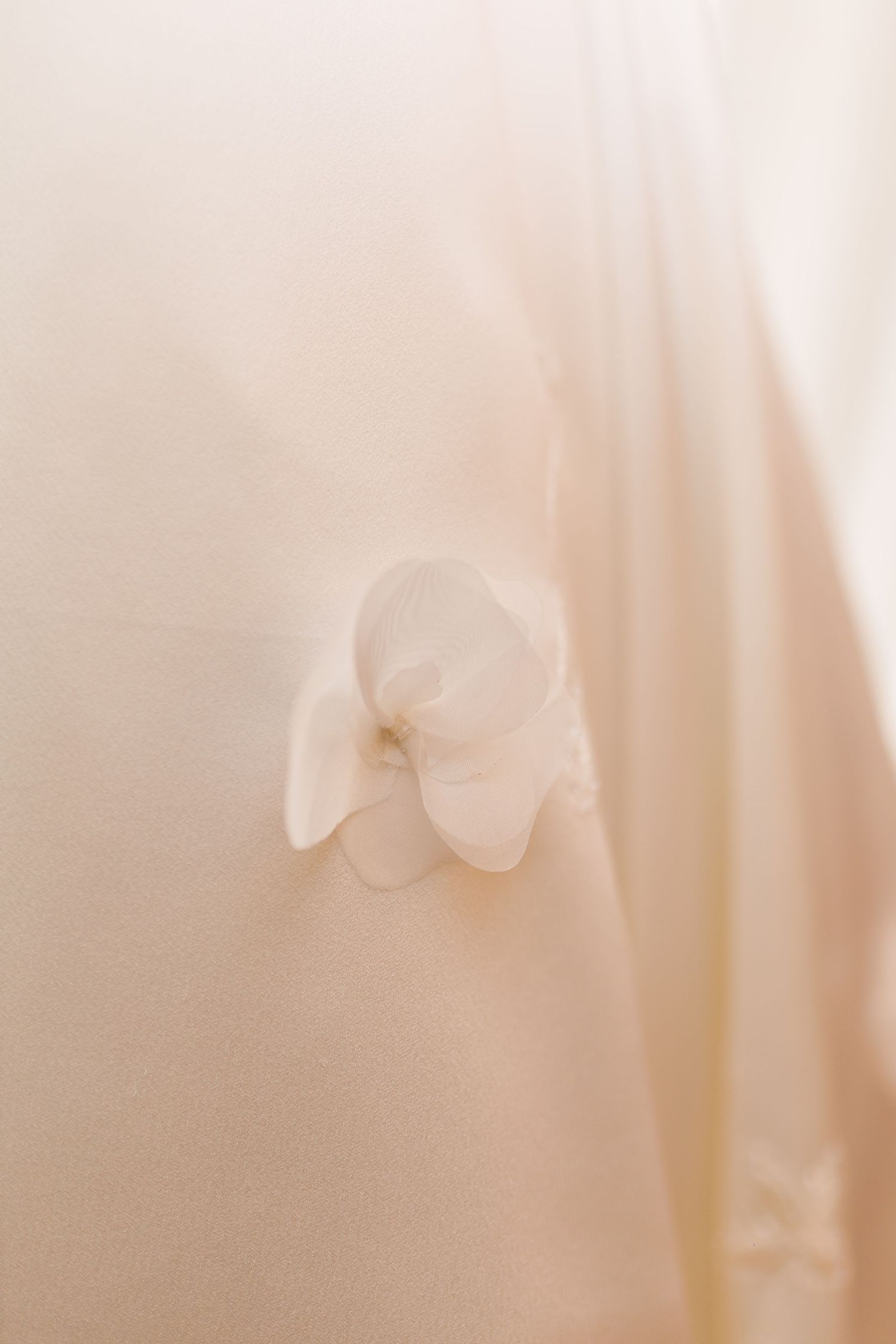 Delicate white fabric flower embellishment on soft blush silk wedding dress fabric.