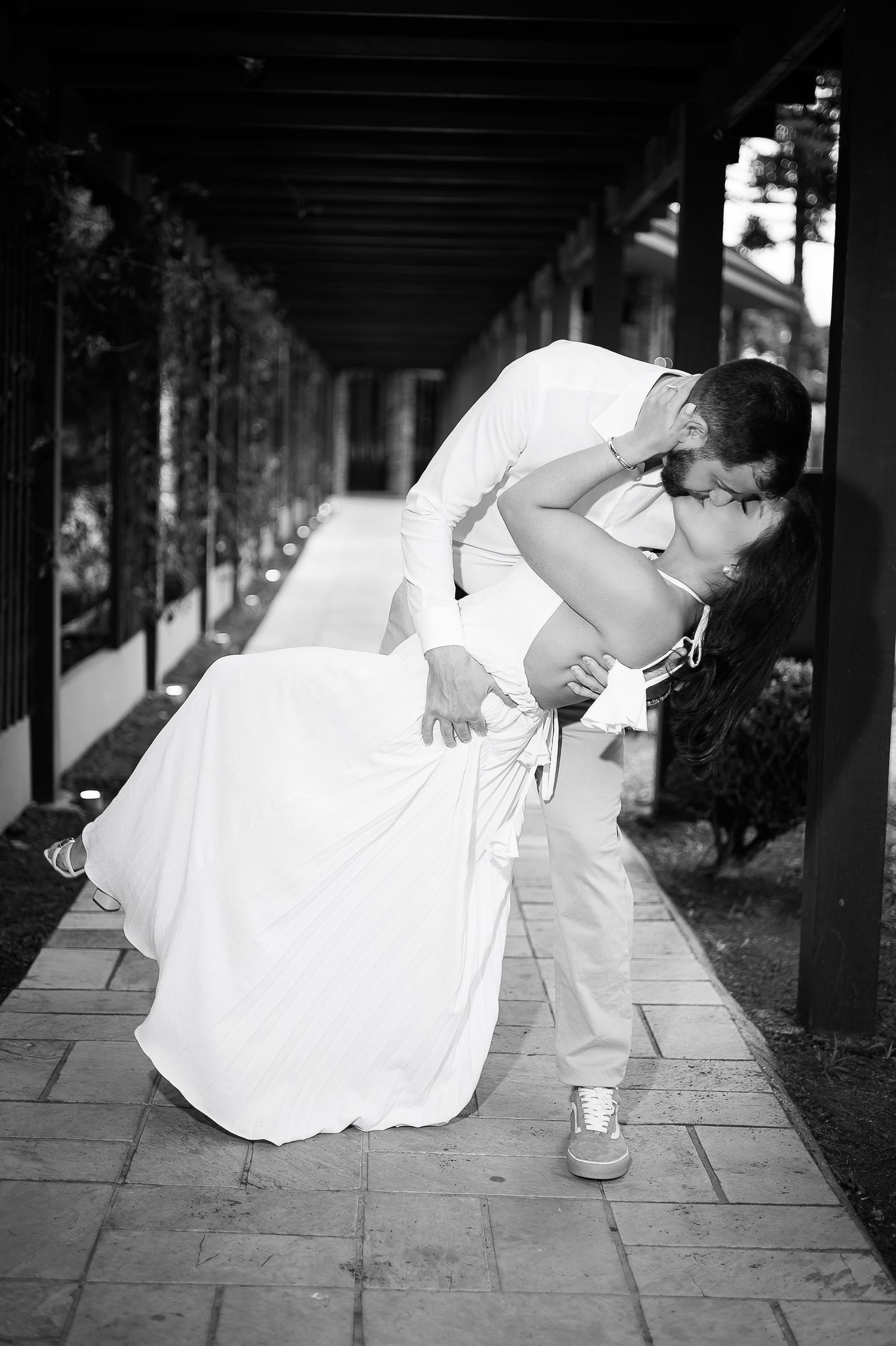 Black and white photo of a groom dipping his bride for a kiss in an outdoor corridor on their wedding day.