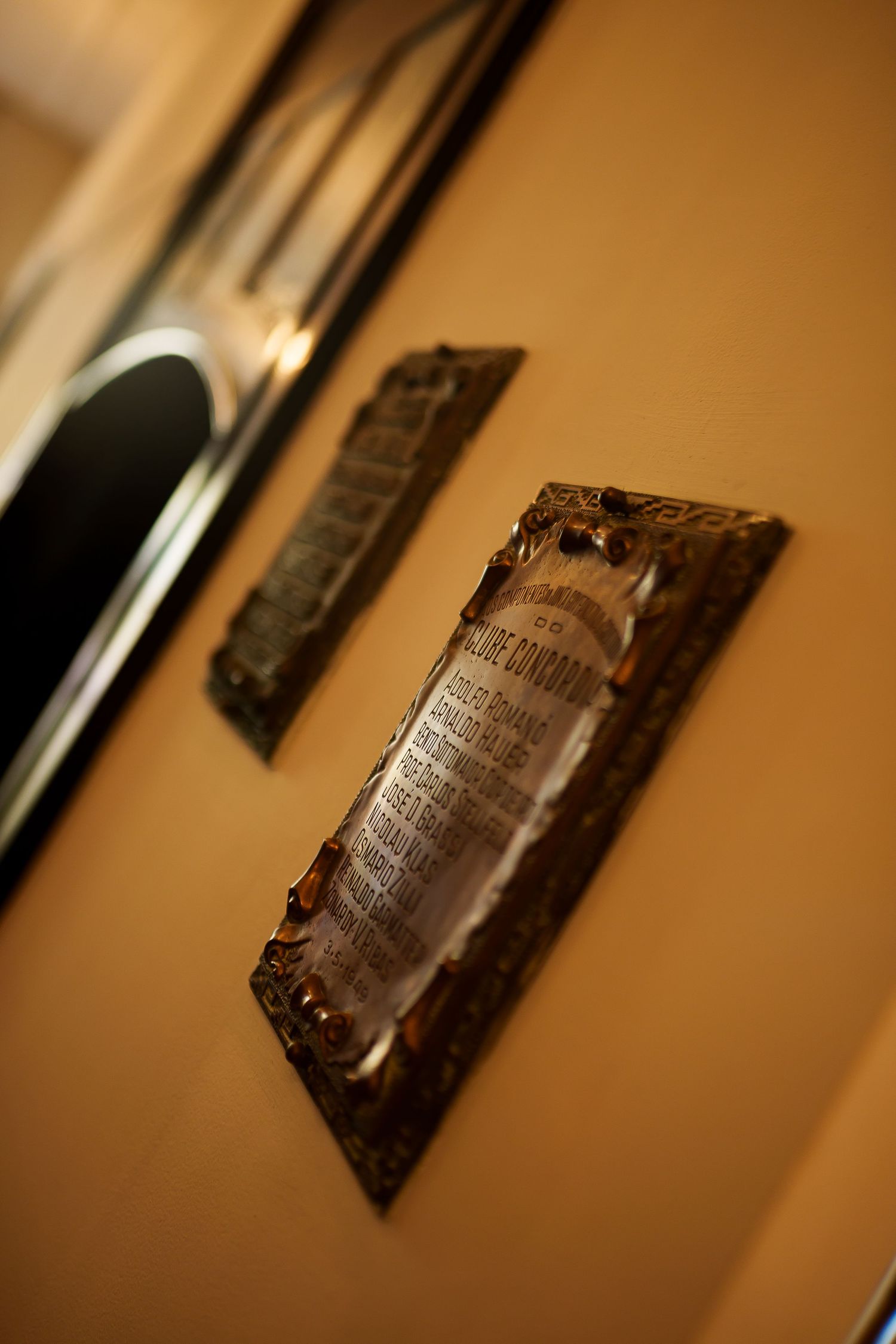 Ornate framed vintage plaques with decorative borders displayed on a warm golden-yellow wall beside a mirror.