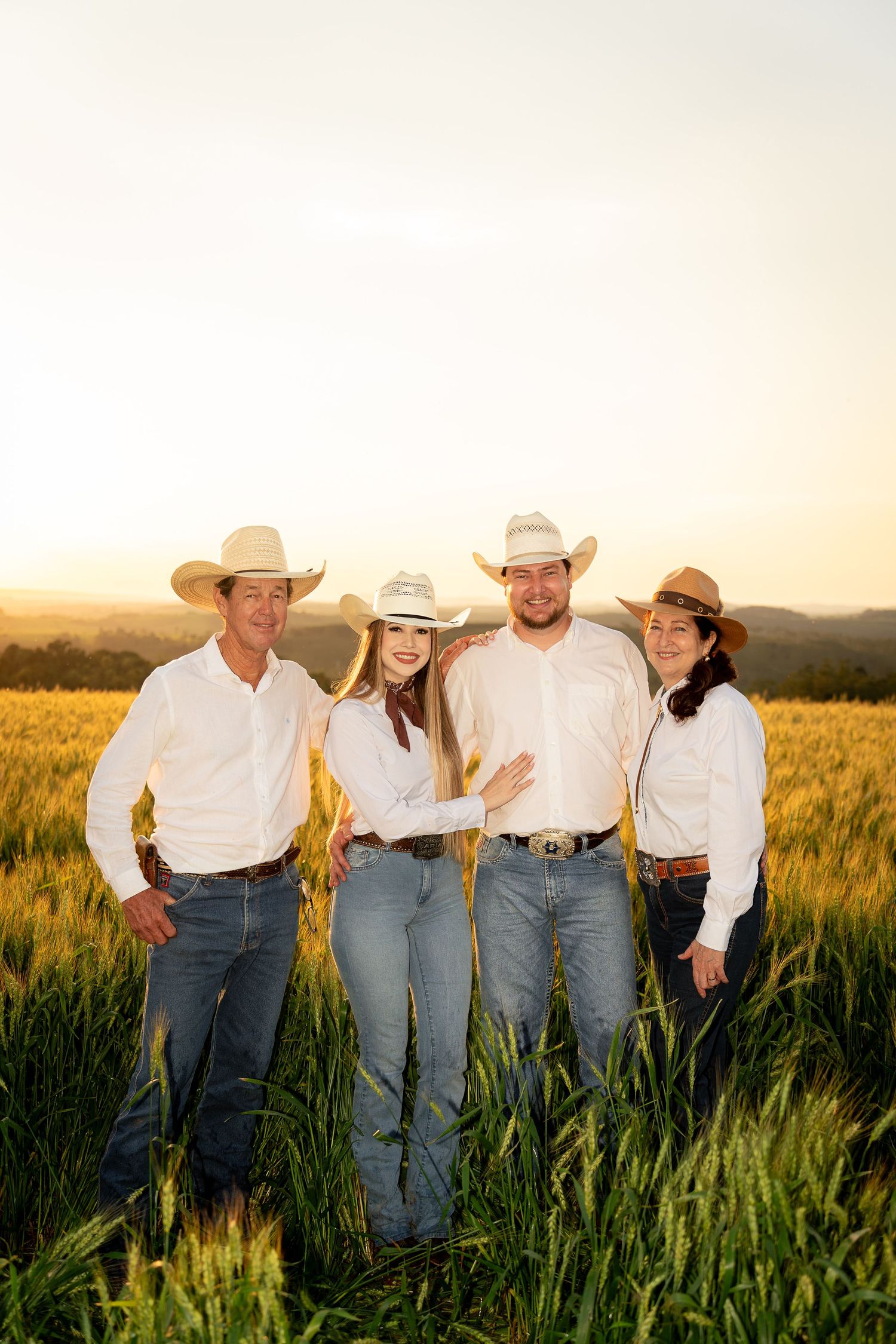 Four people in cowboy hats and white shirts pose in a golden wheat field at sunset.