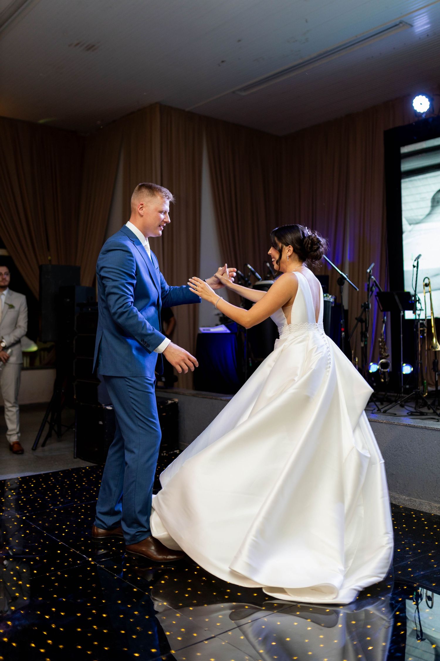 Bride in white ball gown and groom in blue suit share their first dance at an elegant wedding reception.