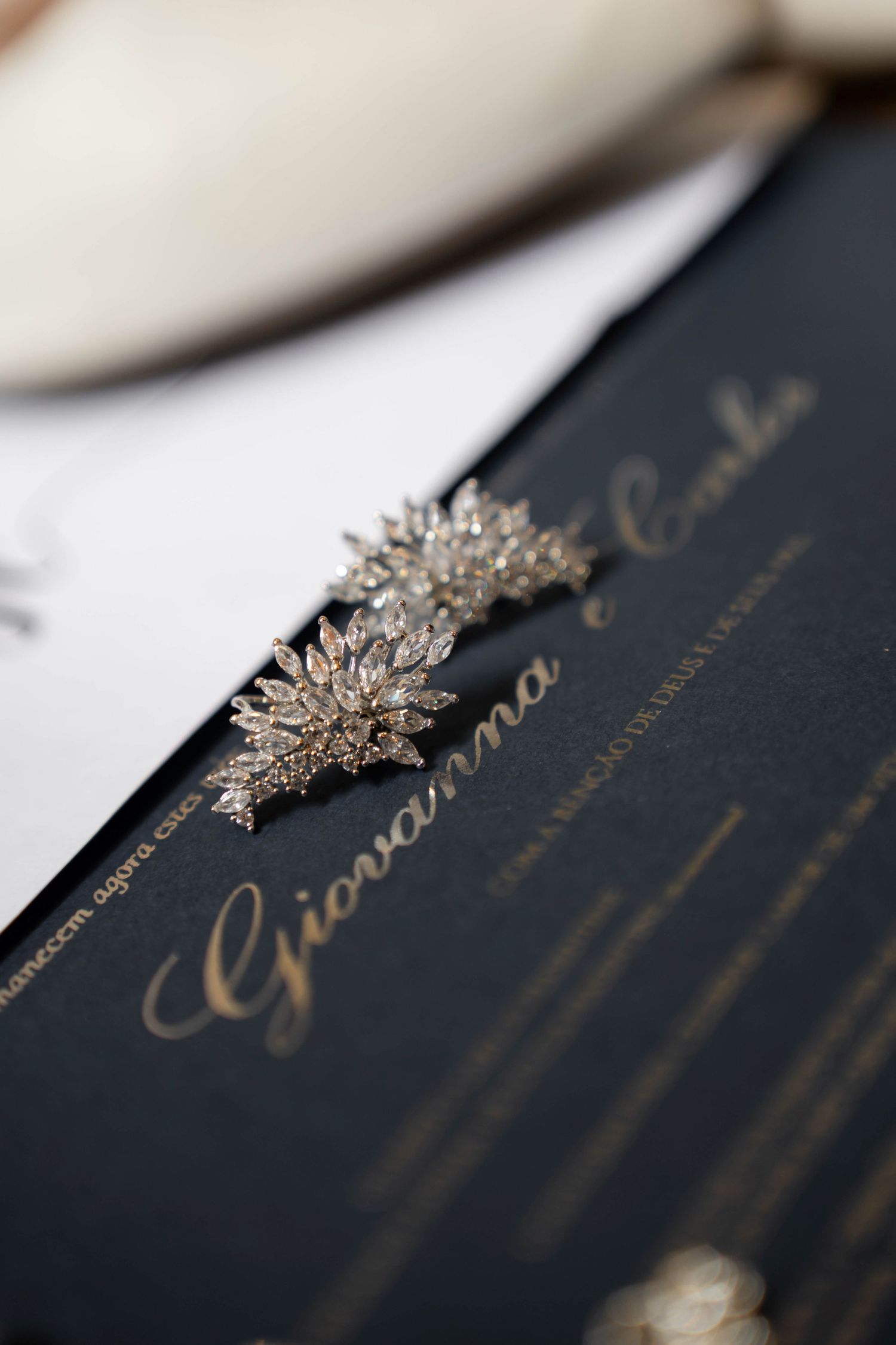 Elegant crystal floral earrings resting on a dark navy wedding invitation with gold script reading Giovanna.