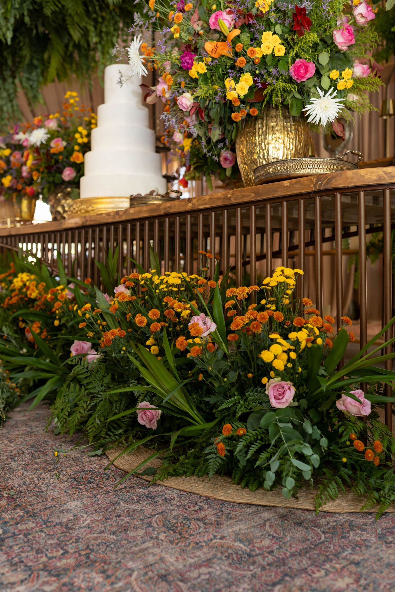 Elegant wedding cake display with colorful floral arrangements of orange, pink, and yellow blooms on a decorated table.