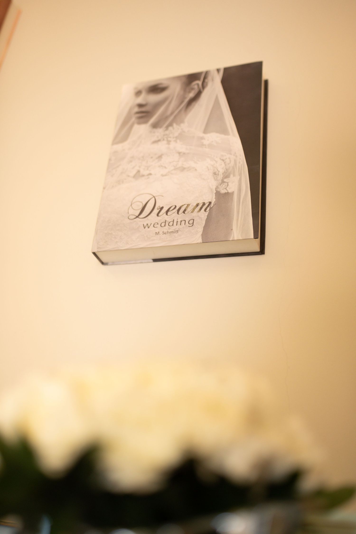 Black and white Dream Wedding book displayed on a cream wall above blurred white roses.
