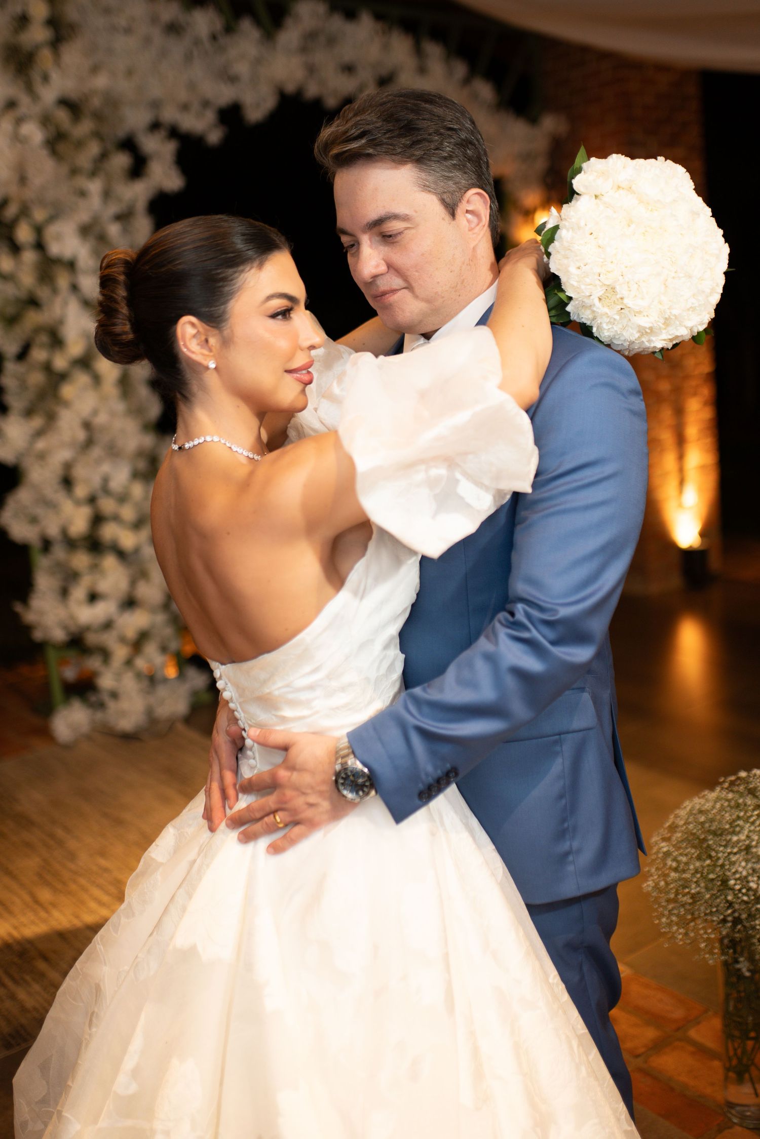 Bride in white strapless gown and groom in blue suit share a romantic first dance embrace at elegant wedding reception.
