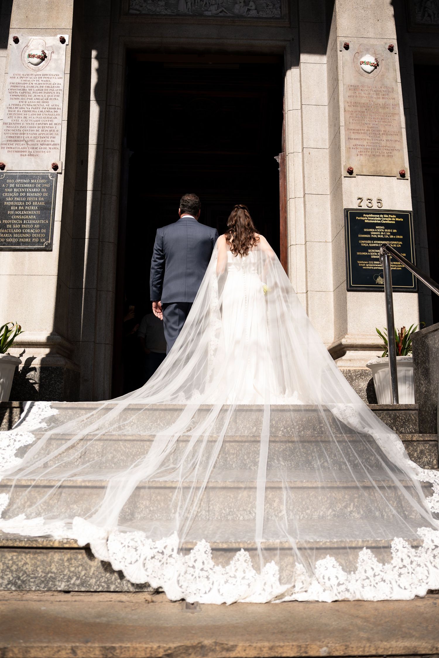 Bride and groom entering a church, bride wearing a stunning long lace cathedral veil trailing down stone steps.