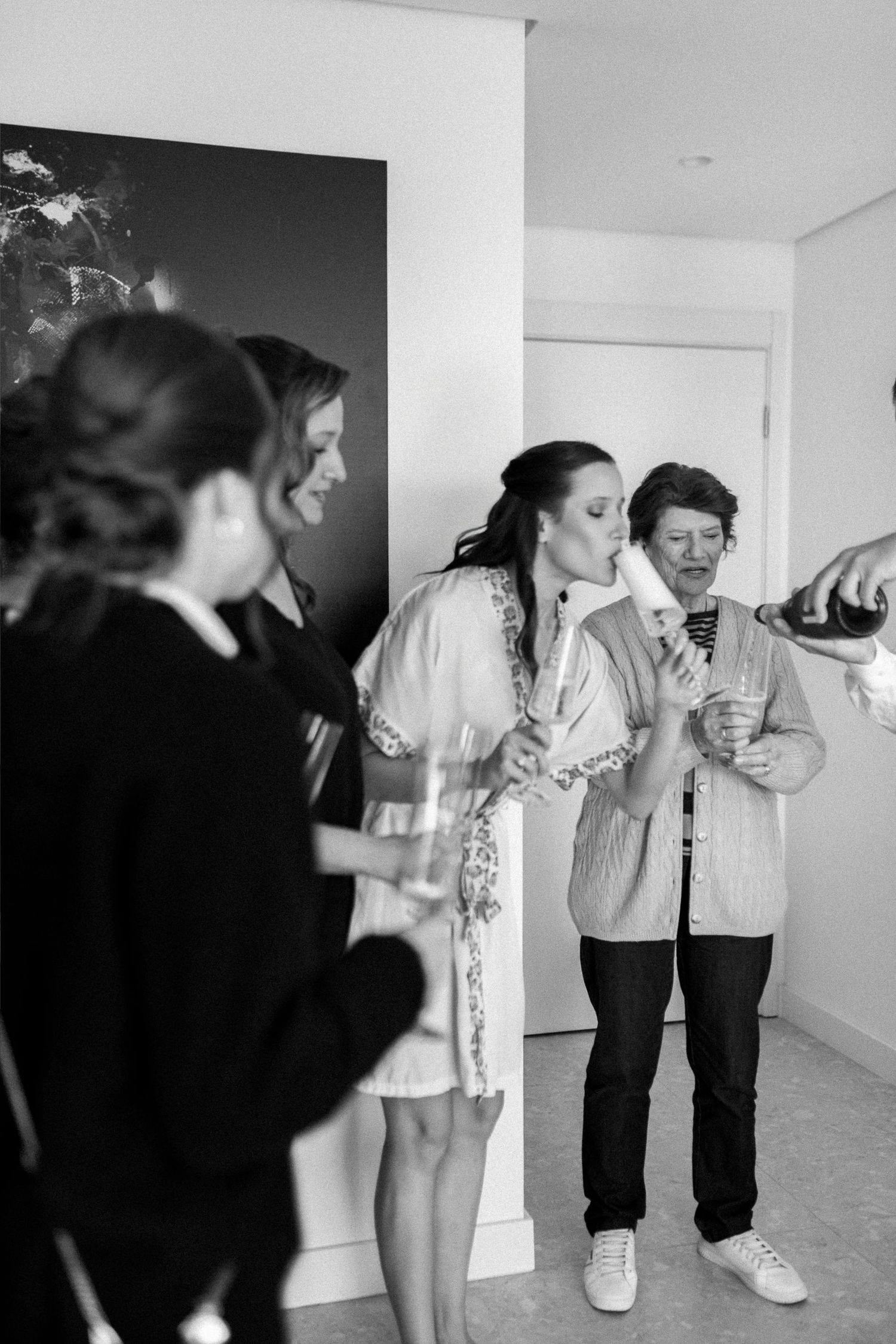 Black and white photo of women celebrating with champagne during a bridal getting ready party indoors.