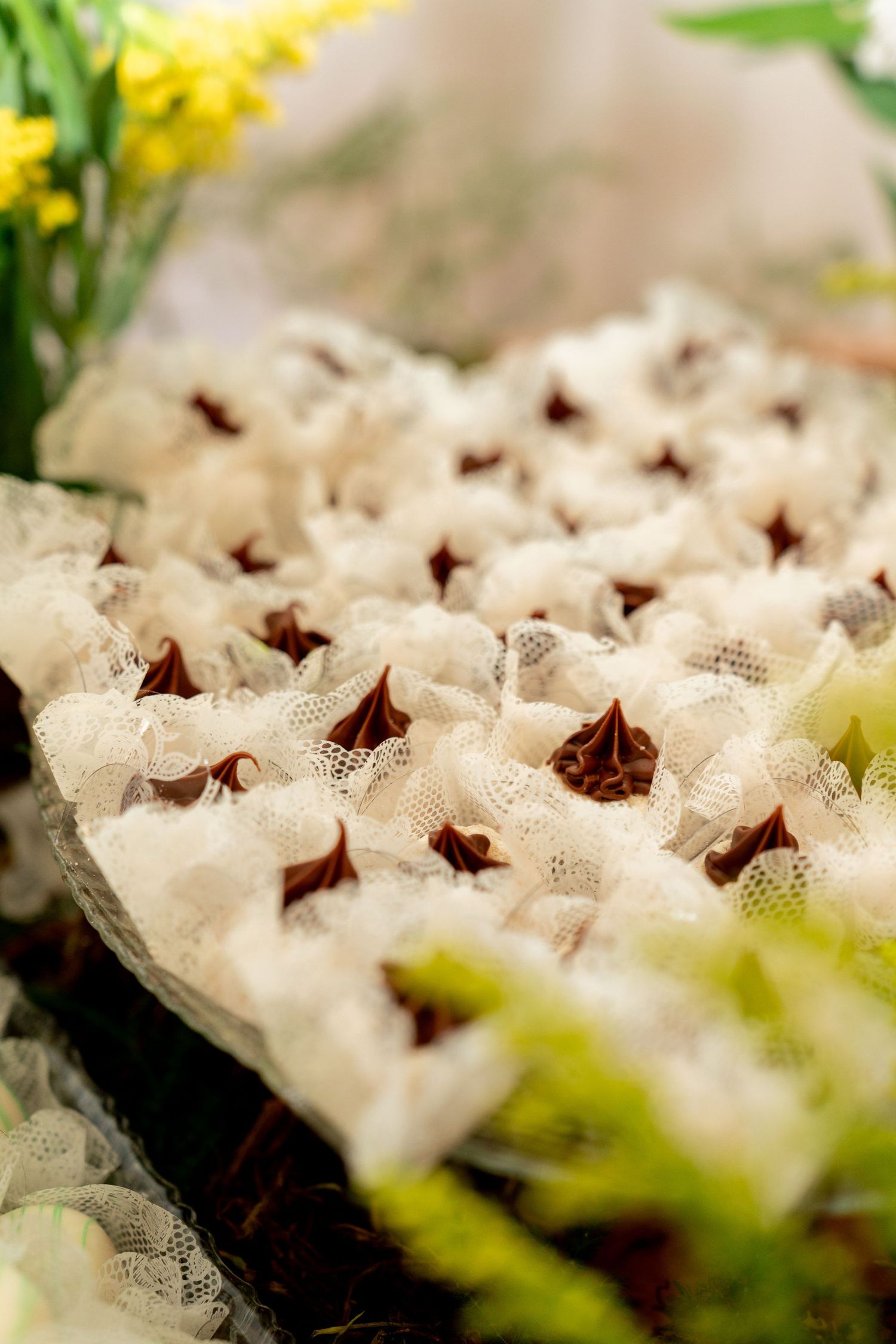 Elegant chocolate truffles wrapped in white lace displayed on a decorative tray surrounded by fresh flowers.