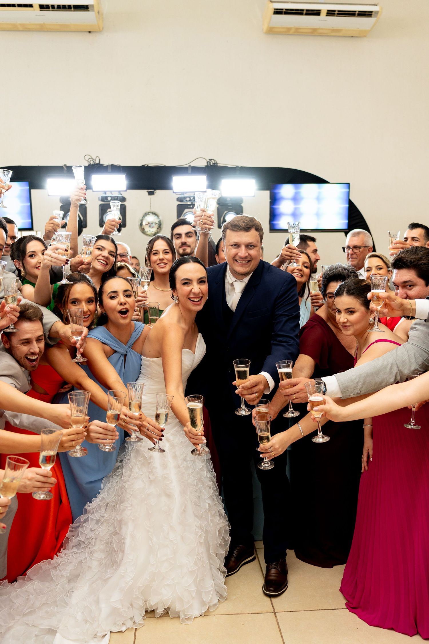 Bride and groom celebrate with wedding guests raising champagne glasses in a joyful group toast at their reception.