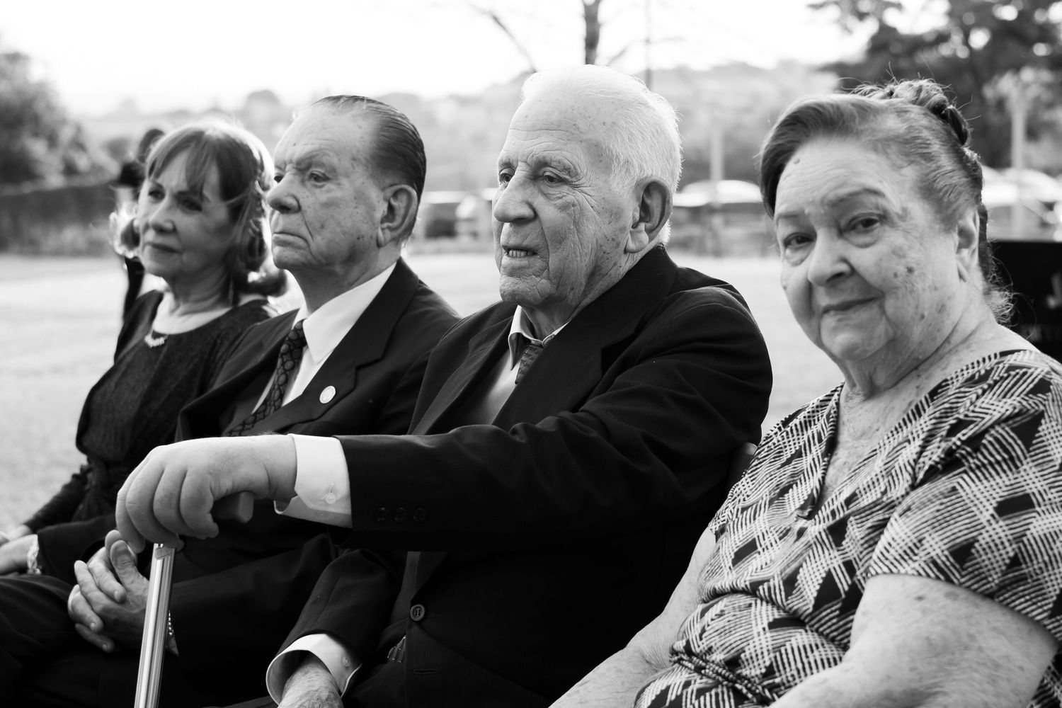 Four elderly wedding guests seated together captured in a candid black and white photograph outdoors.