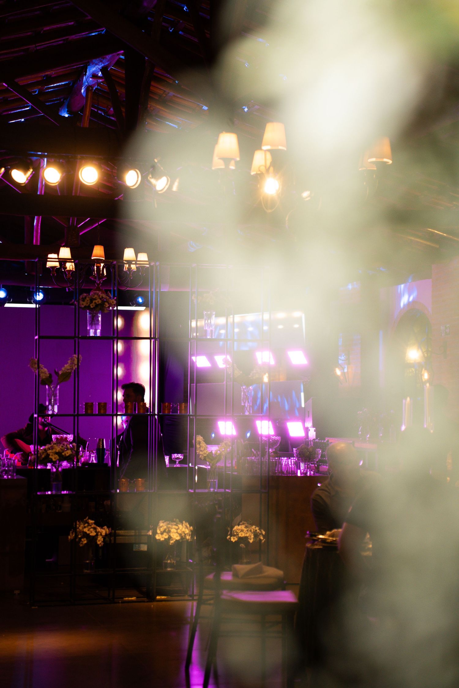 Elegant event venue with purple lighting, chandeliers, stage lights, and floral arrangements creating a dramatic atmosphere.