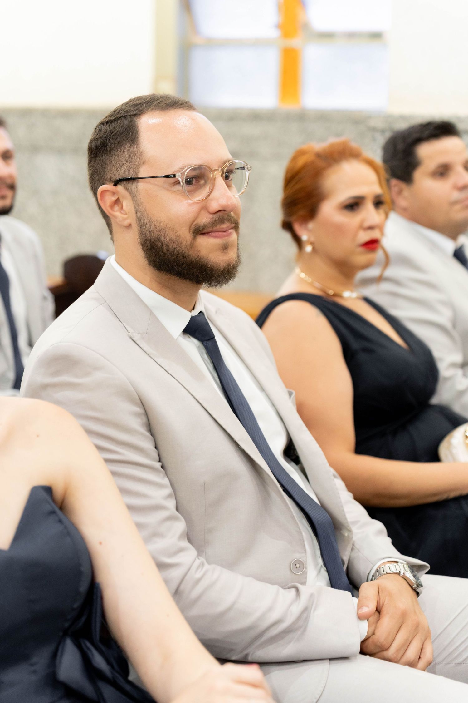 Man in light gray suit and tie with glasses smiling while seated at a formal event.