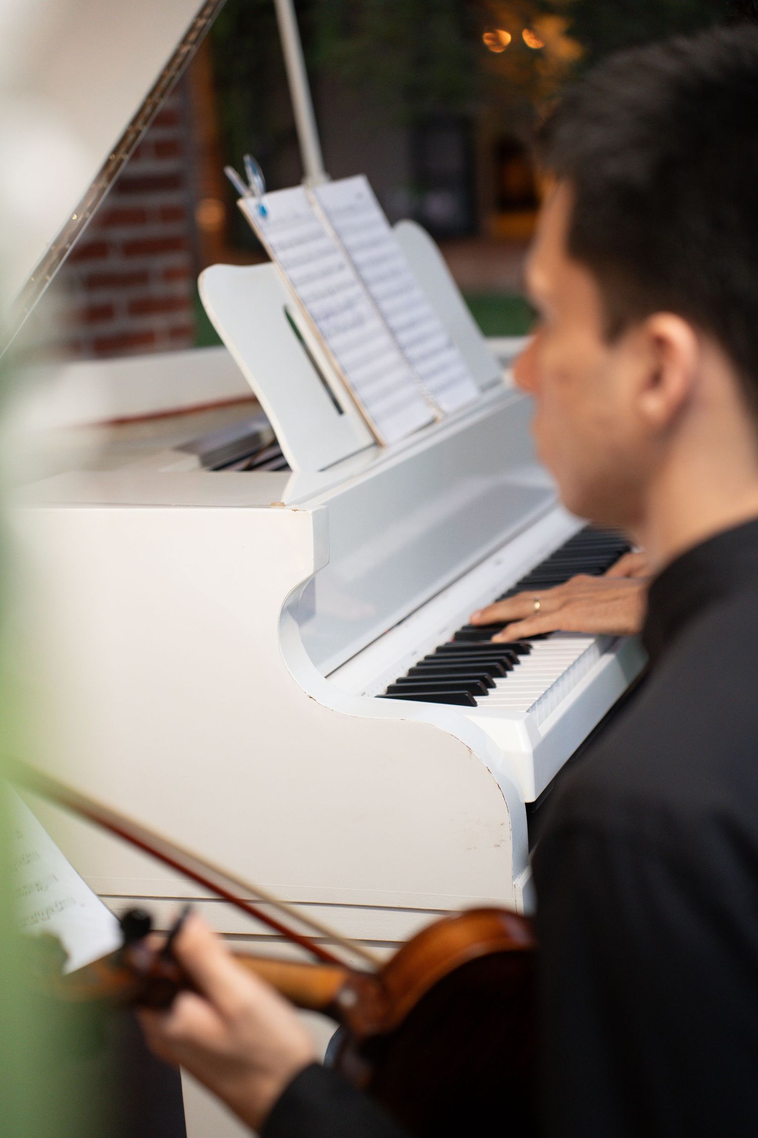 Musician playing violin beside a white grand piano with sheet music, performing at an elegant outdoor event.