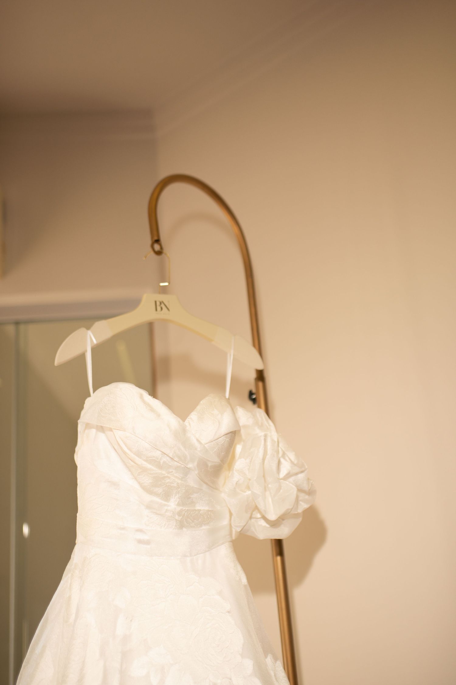 White strapless wedding dress with sweetheart neckline hanging on a personalized wooden hanger on a gold rack.