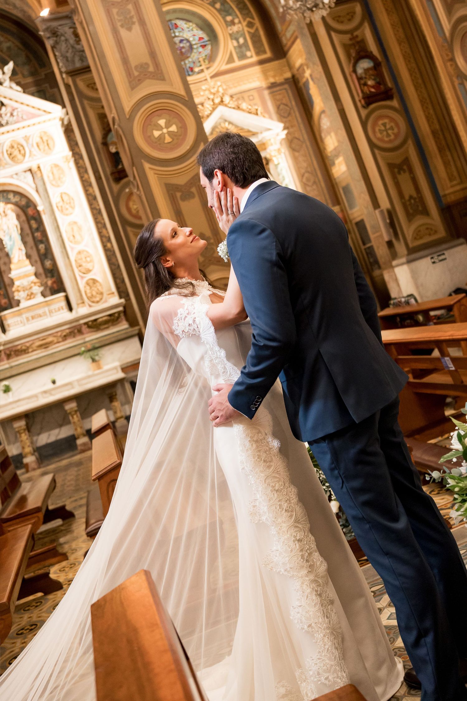 Bride and groom share a romantic first kiss at the altar of an ornate church during their wedding ceremony.