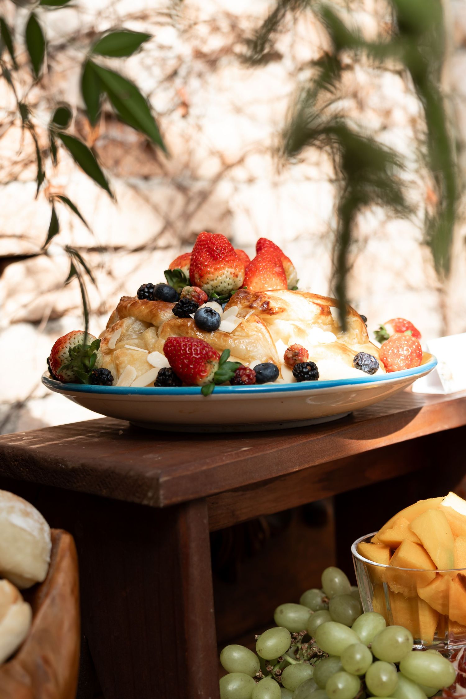 A elegant dessert plate topped with fresh strawberries and blueberries beside grapes on a rustic wooden table outdoors.