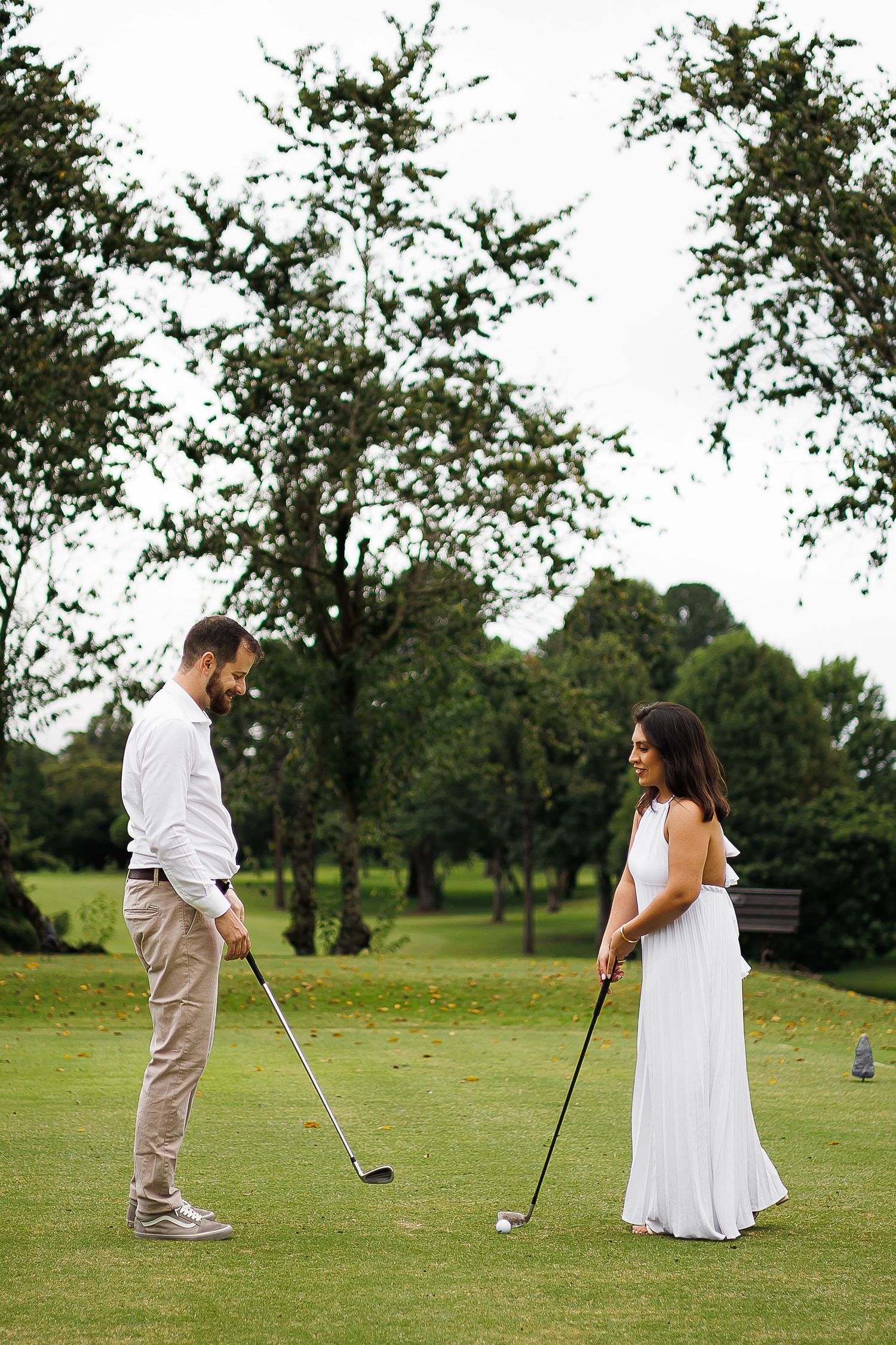 Couple dressed elegantly playing golf on a lush green course, man in white shirt and woman in white dress.