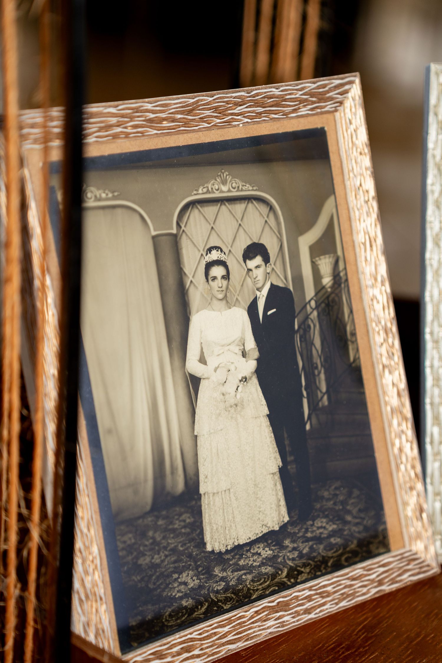 Vintage black and white wedding portrait in ornate frame showing bride in lace gown and groom in suit.