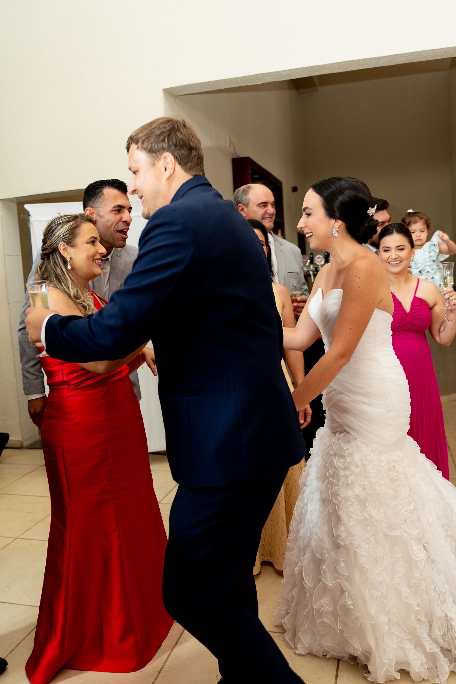 Bride and groom dance joyfully with guests in red and pink dresses at wedding reception.