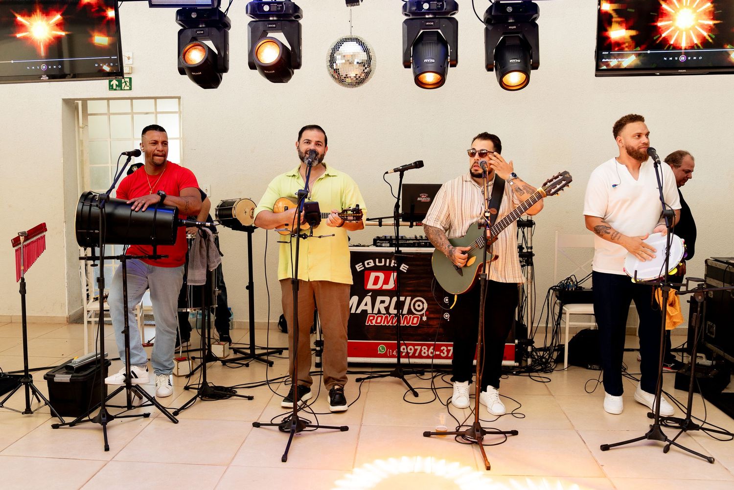 Live band performing on stage with guitars, microphones, and stage lighting at an indoor music event.