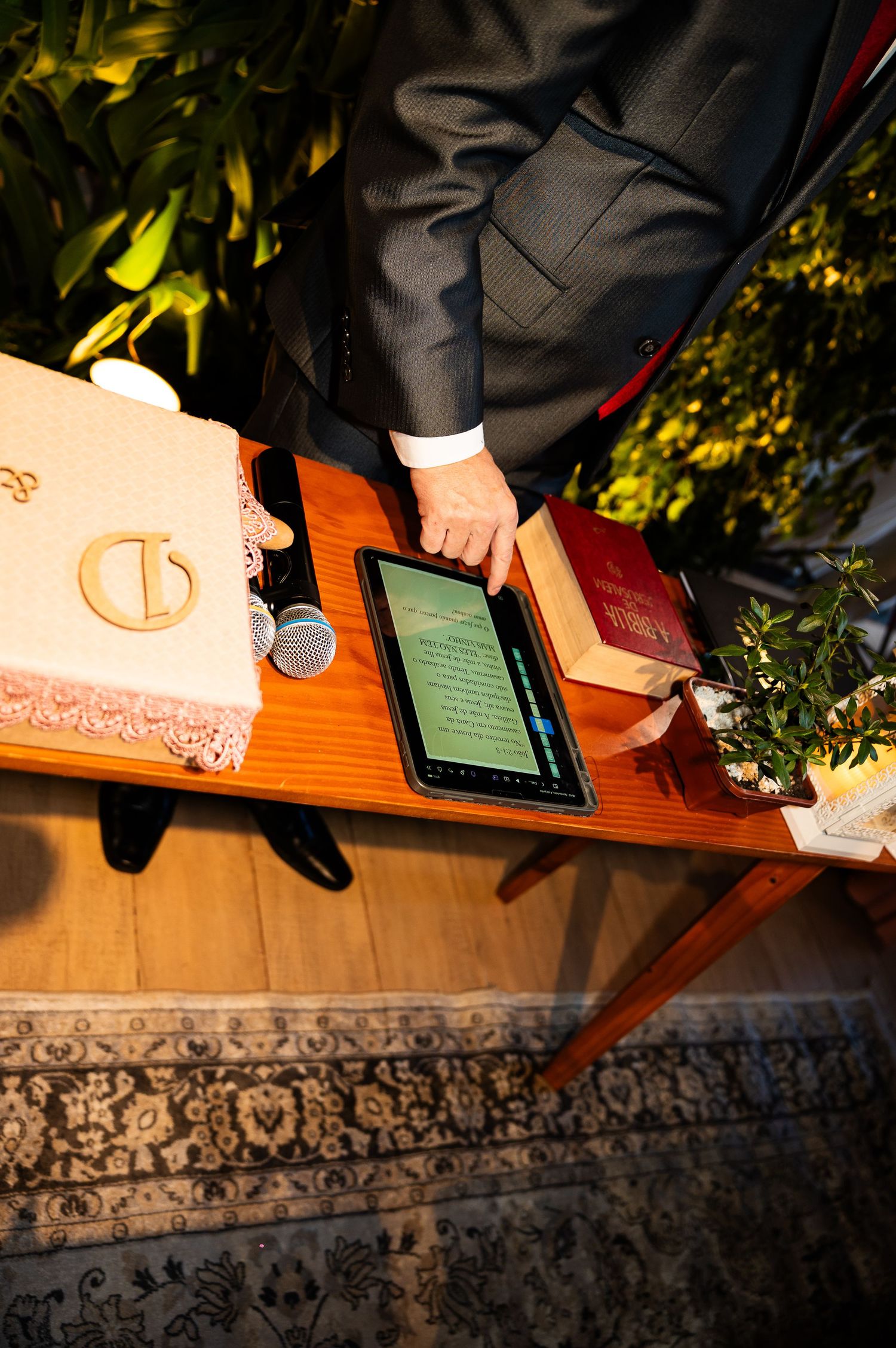 Officiant using a tablet at a wooden altar with wedding rings, microphone, and books during a ceremony.