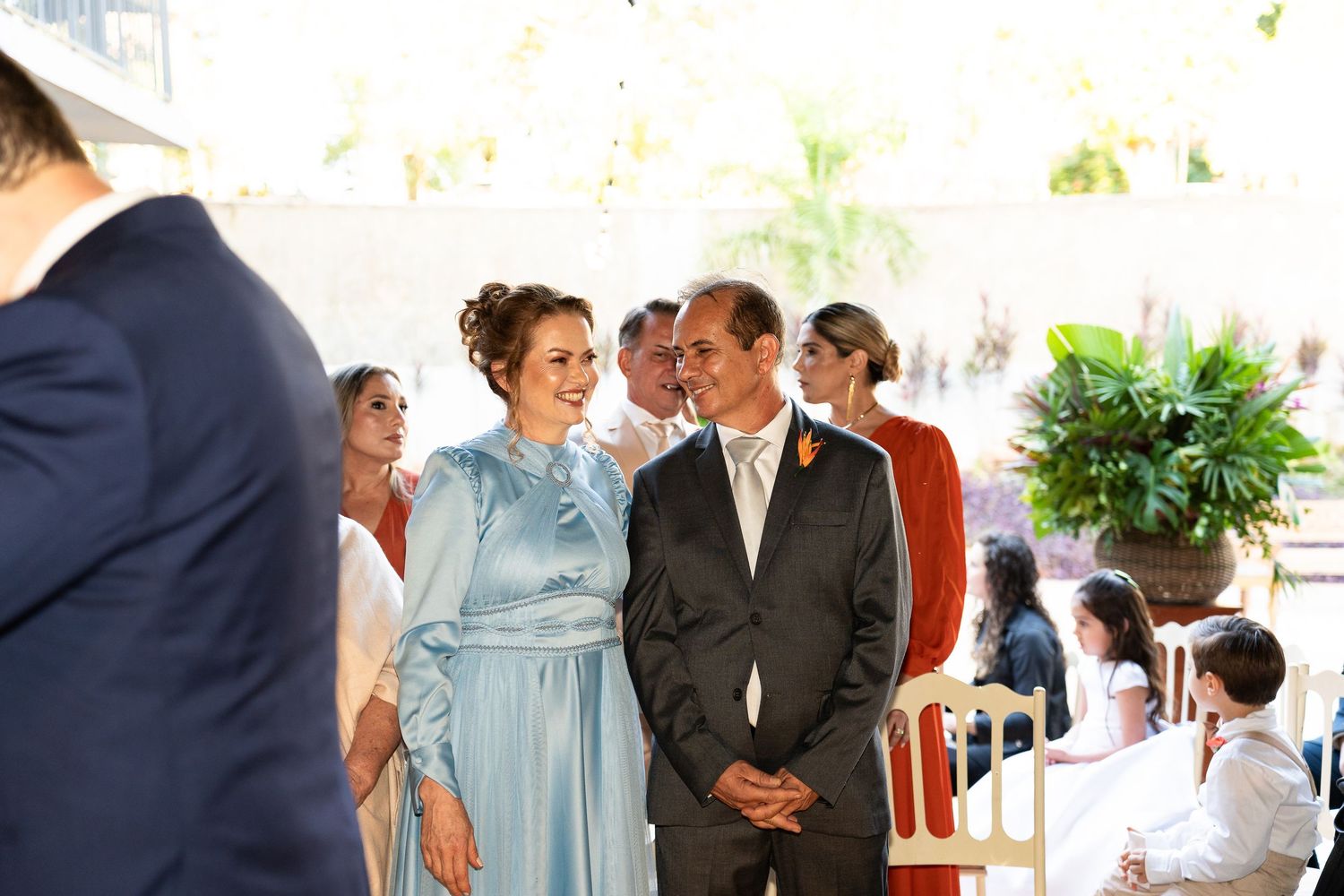 Smiling bride in blue satin dress and groom walking down the aisle at outdoor wedding.
