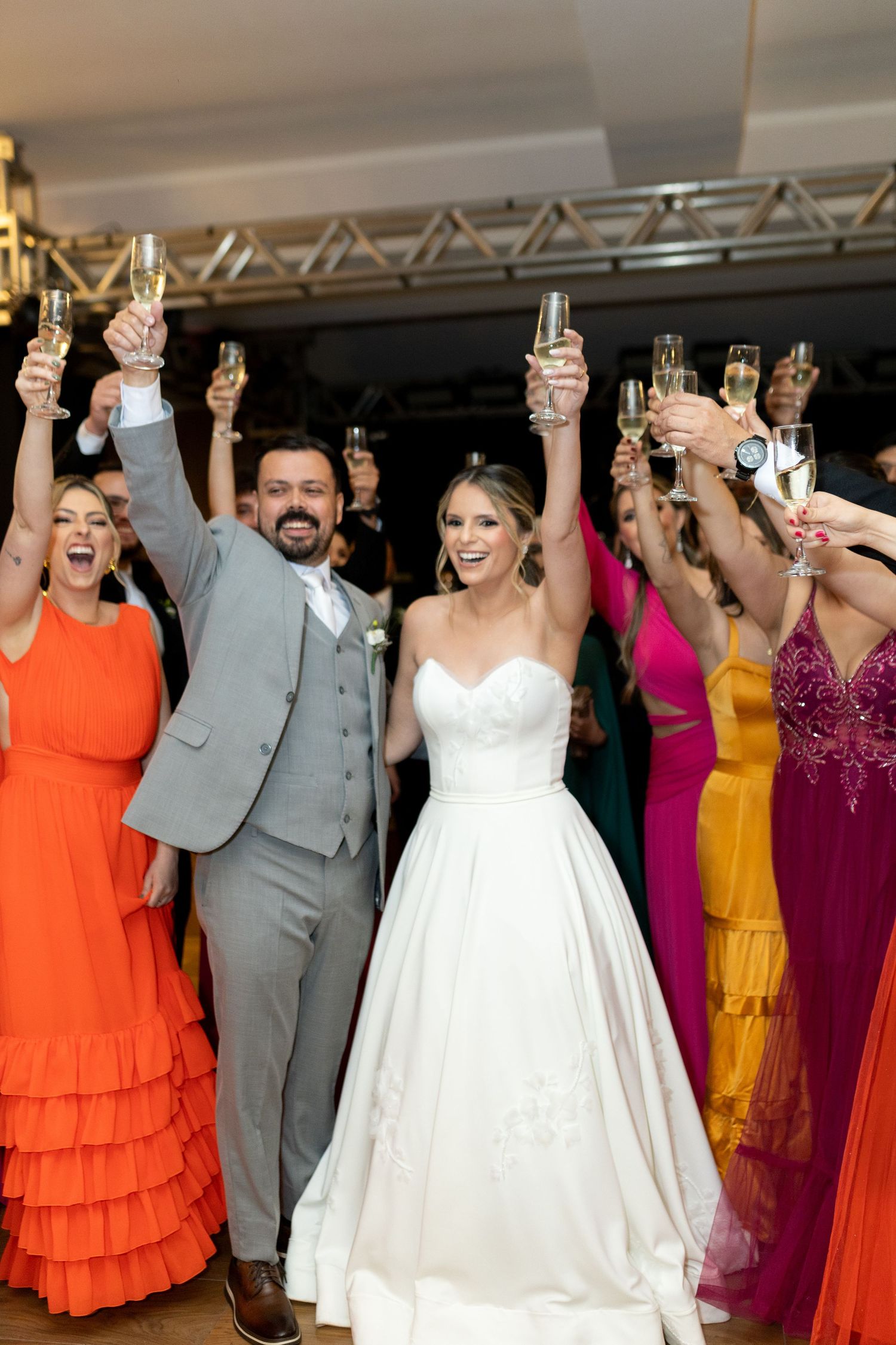 Bride and groom raise champagne glasses with colorfully dressed wedding guests during a joyful reception toast.