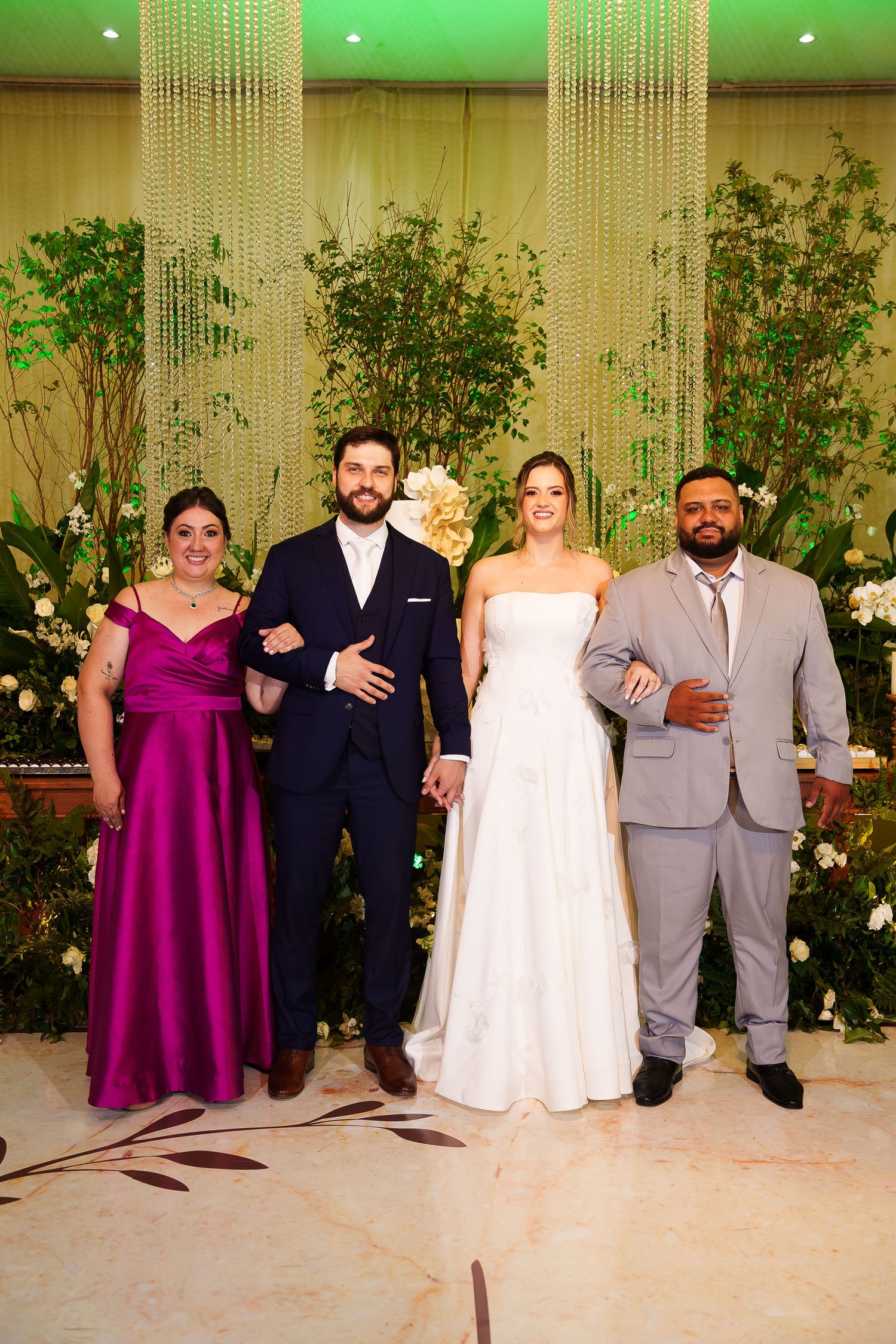 Wedding party of four posing elegantly, bride in white gown, groom in navy suit, guests in magenta dress and gray suit.