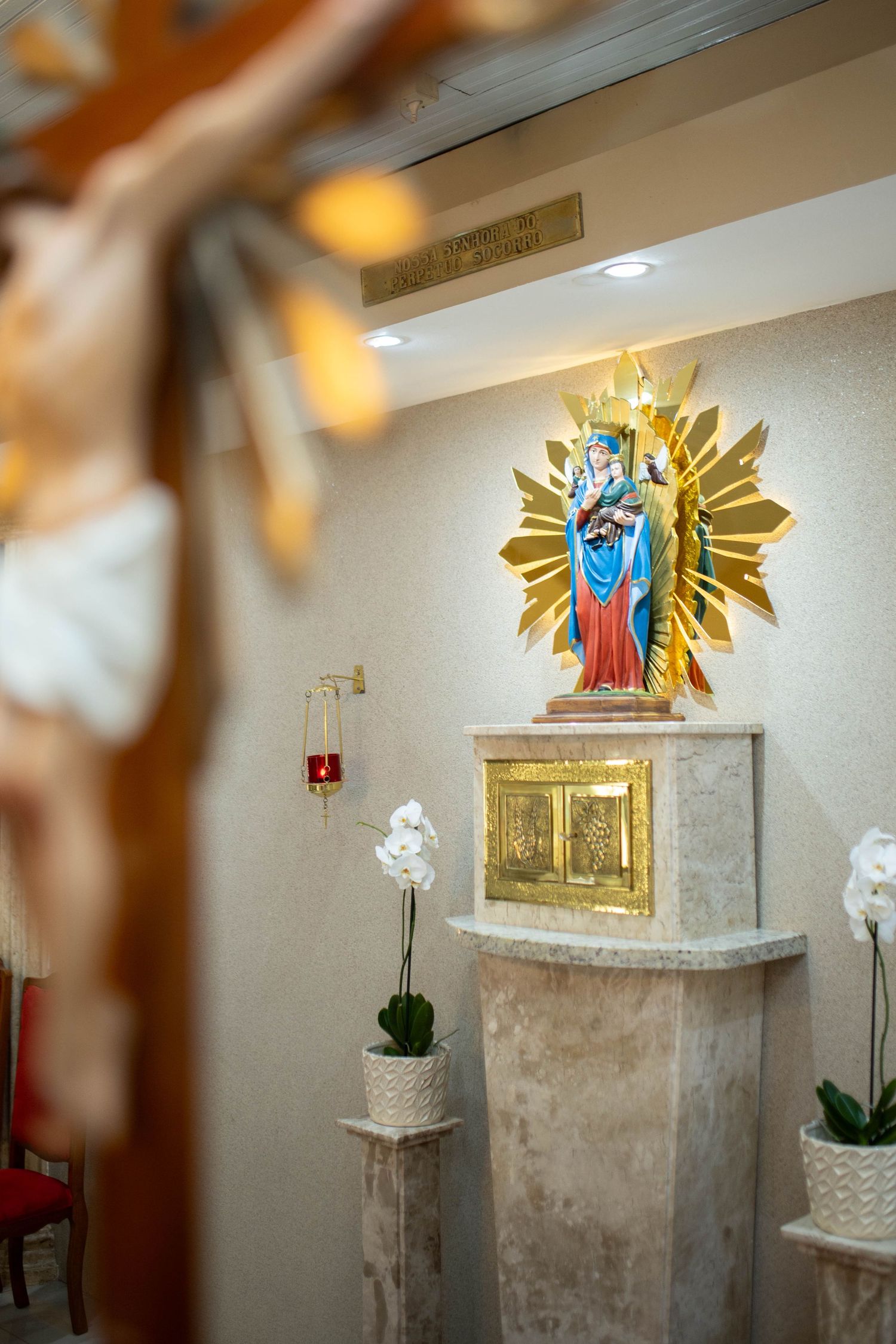 Catholic chapel interior with Virgin Mary statue on golden sunburst altar and crucifix in foreground.