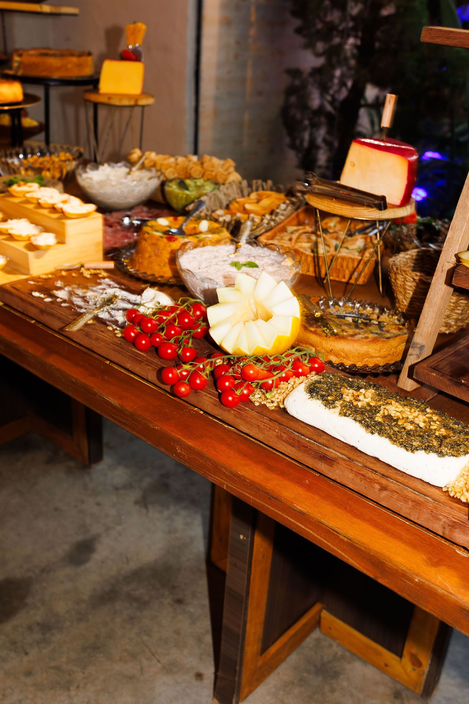 Rustic wooden table displaying a charcuterie spread with cherry tomatoes, cheeses, breads, and assorted appetizers at a catered event.