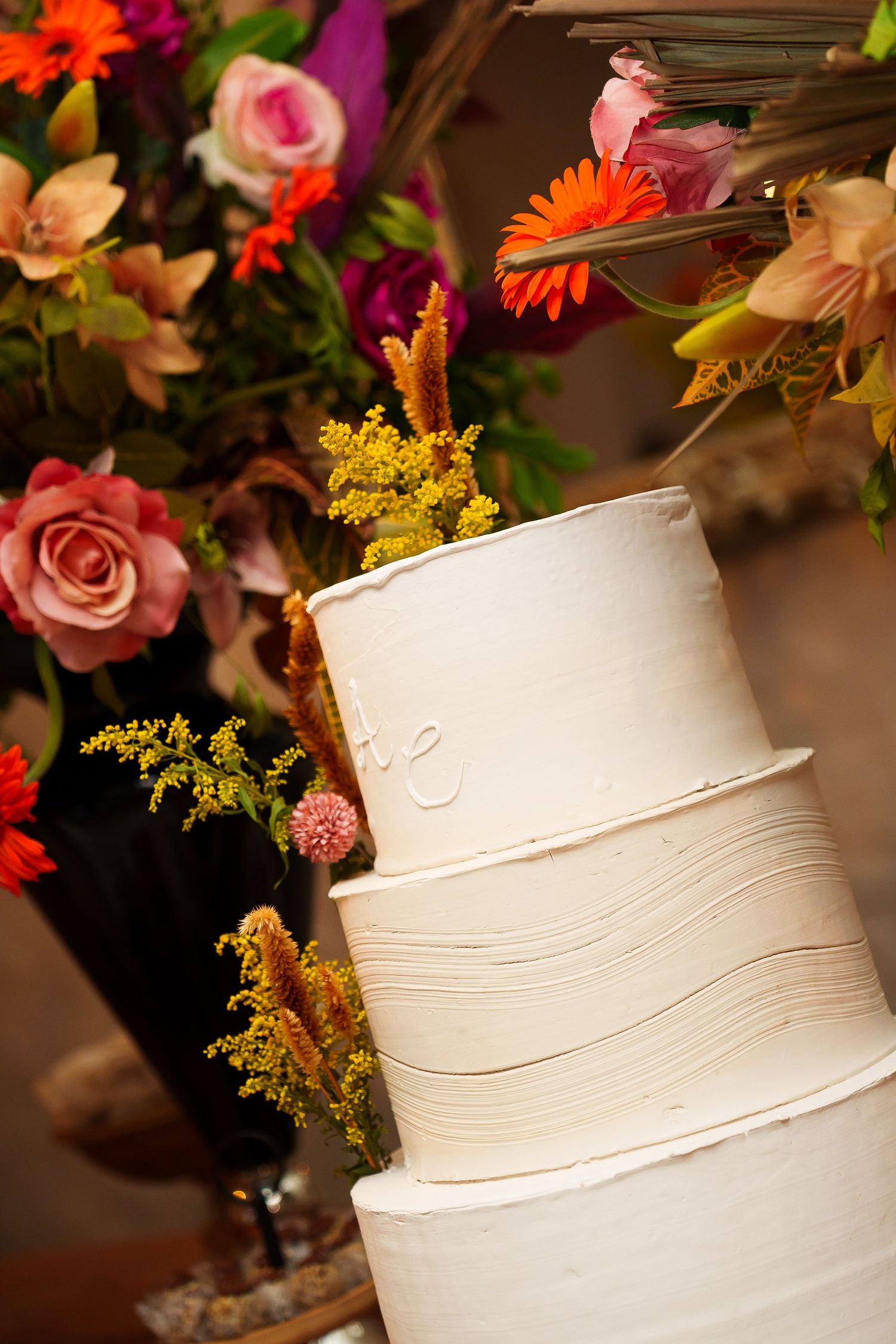 Elegant white three-tier wedding cake with textured frosting displayed beside a vibrant floral arrangement.