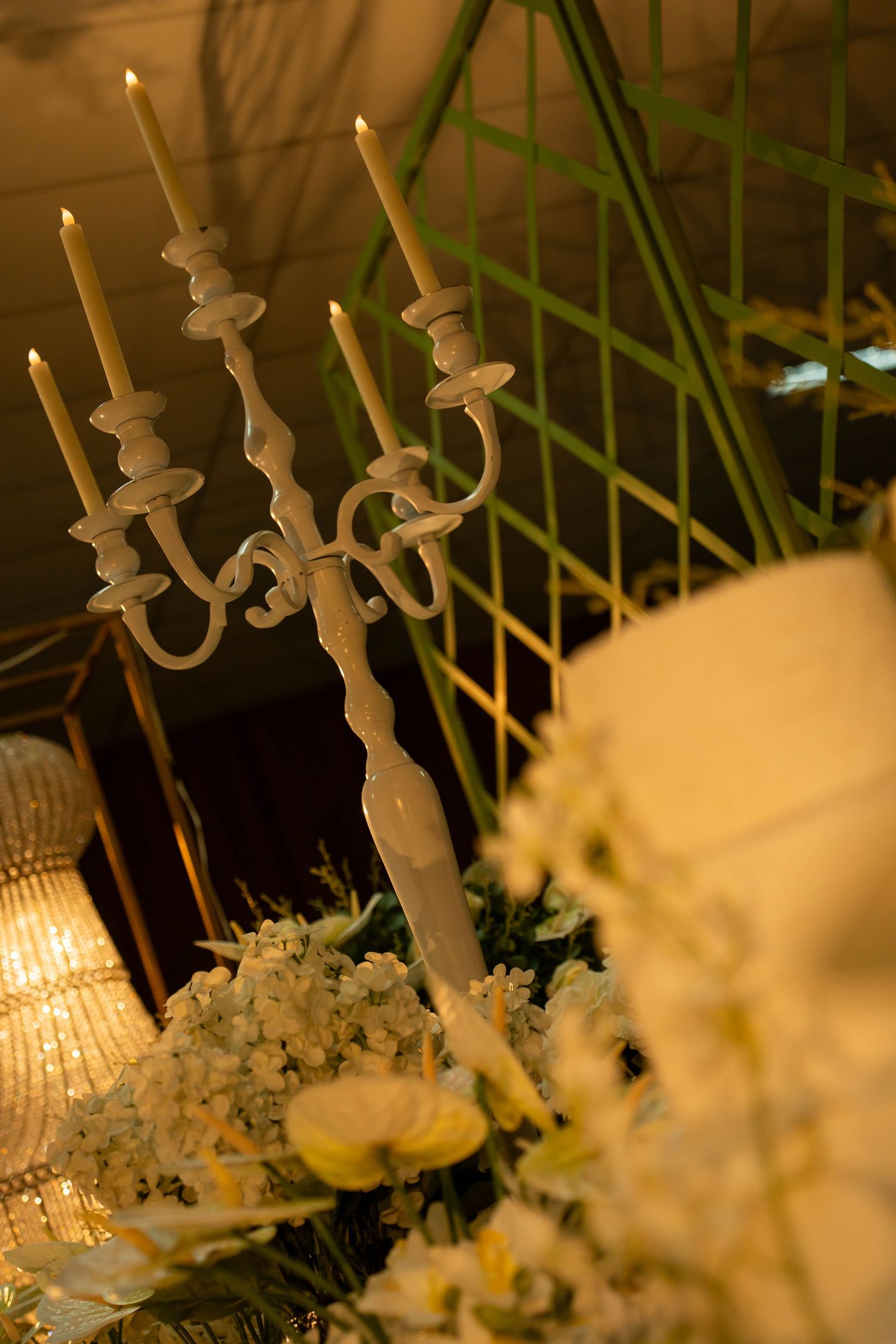 White candelabra with lit candles surrounded by white floral arrangements at an elegant event.
