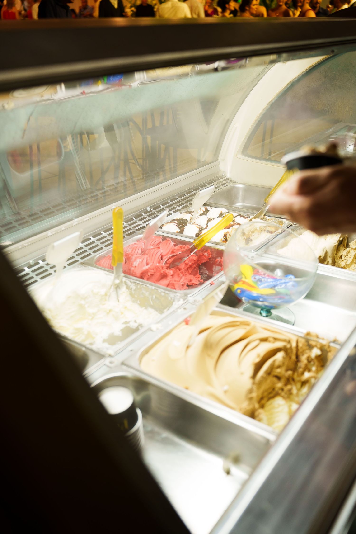 Glass display case at an ice cream shop showing multiple flavors of gelato with serving spoons.