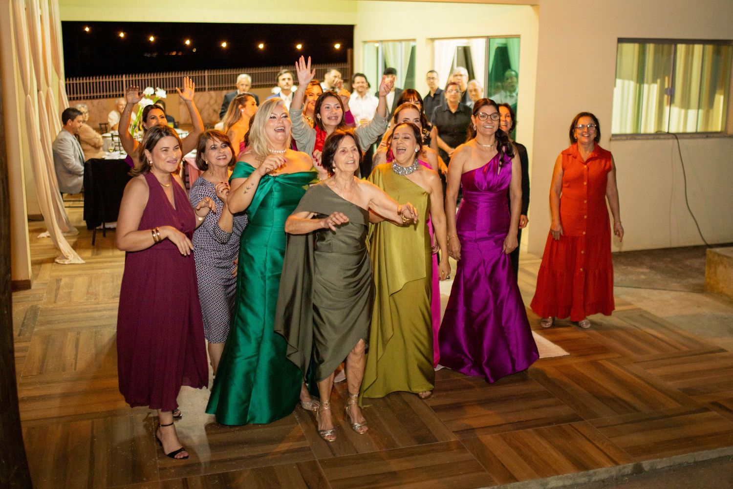Group of elegantly dressed women in colorful gowns posing and celebrating together at a formal event.