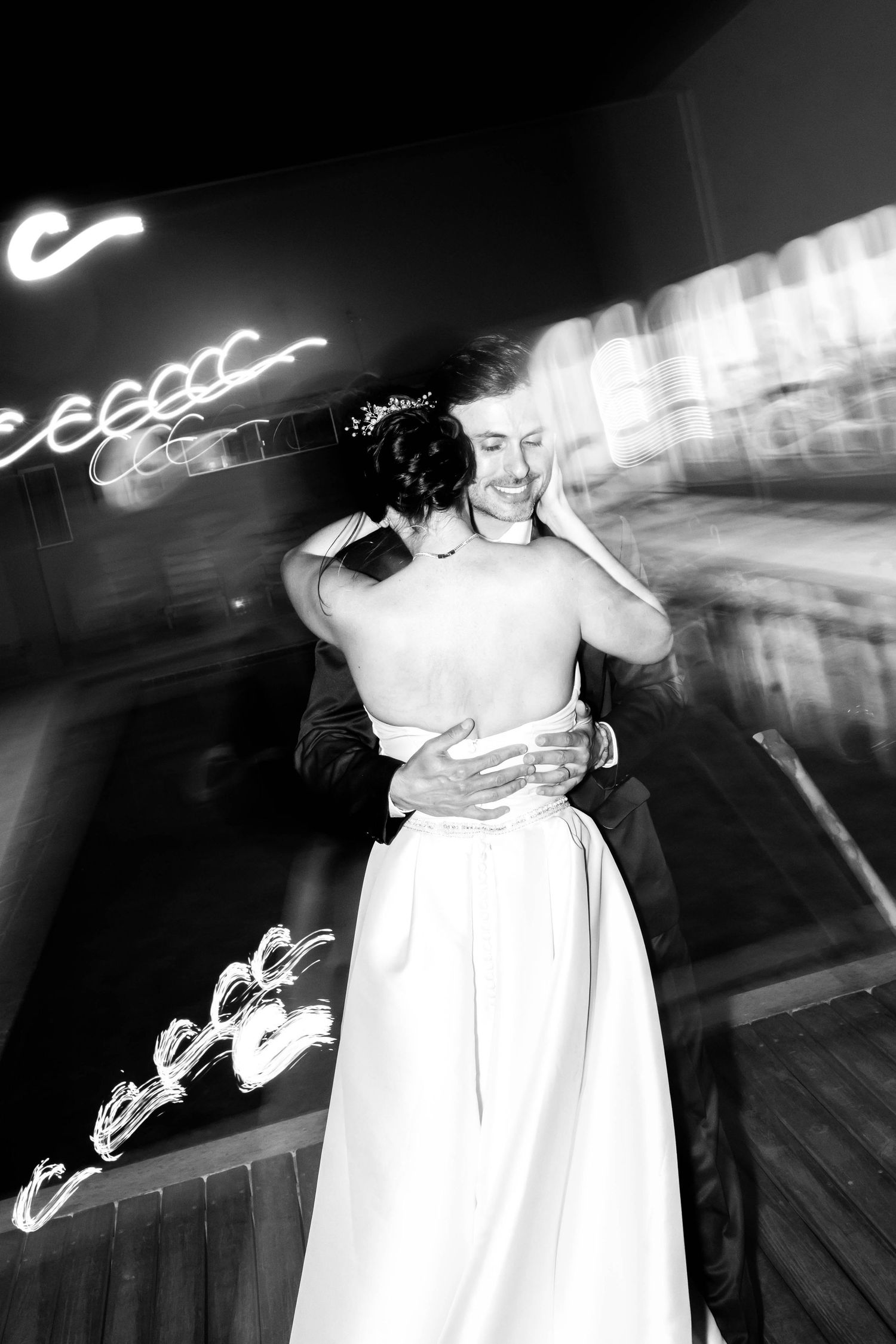 Black and white photo of a smiling groom embracing his bride during their first dance at a wedding reception.