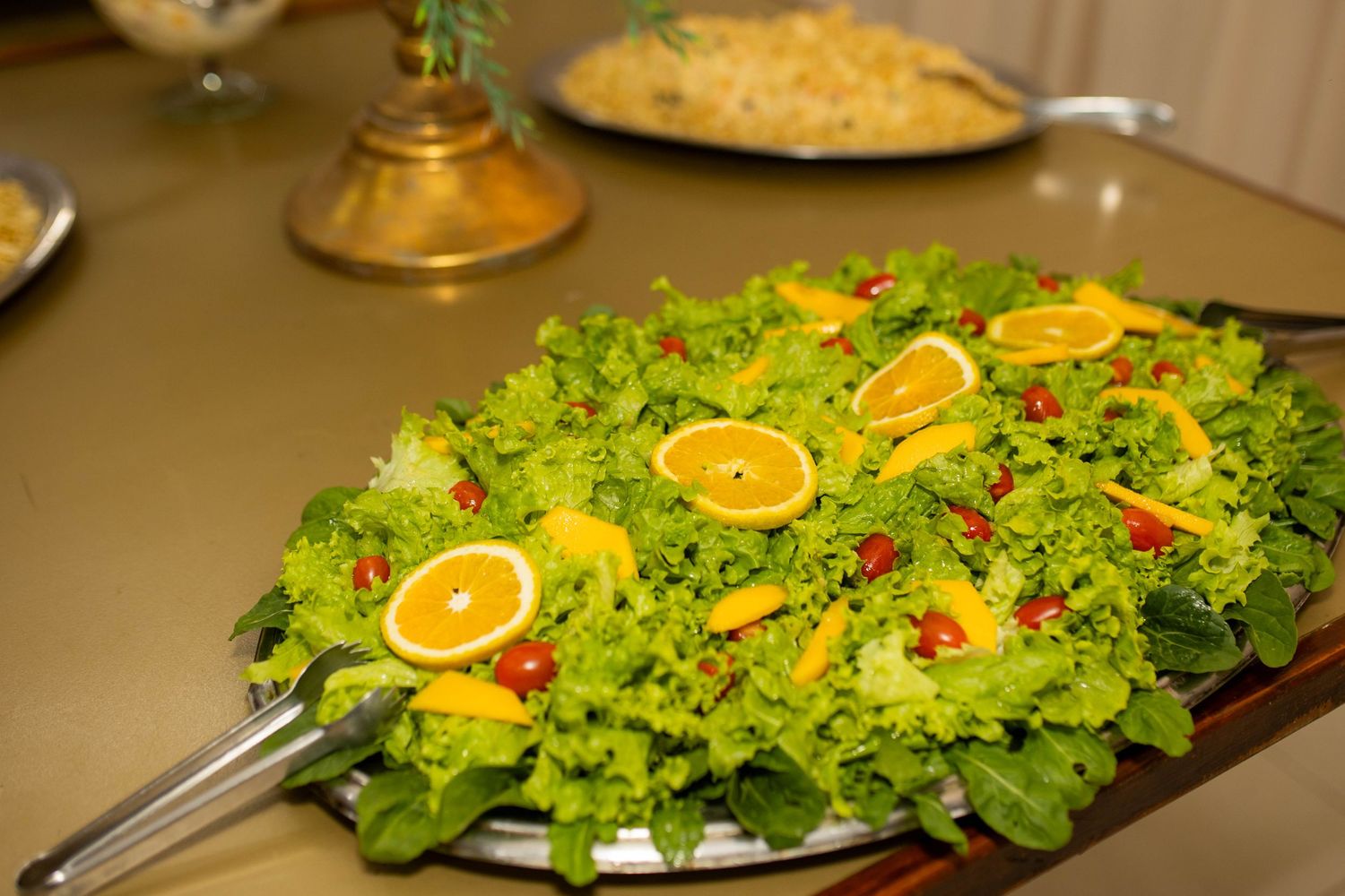 Fresh green salad topped with orange slices and cherry tomatoes served on a large platter at a buffet.