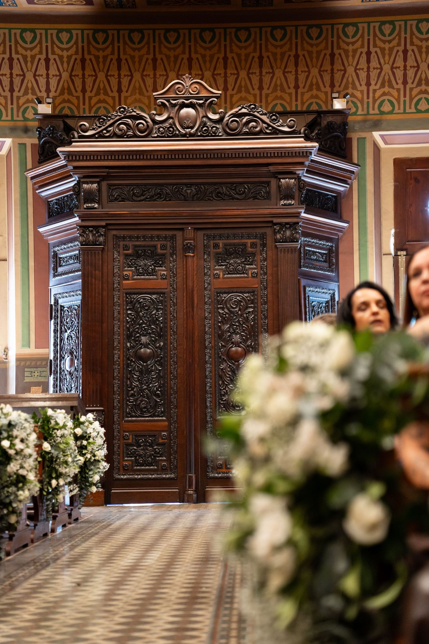 Ornate carved wooden church doors with floral arrangements and decorated ceiling in elegant wedding venue.