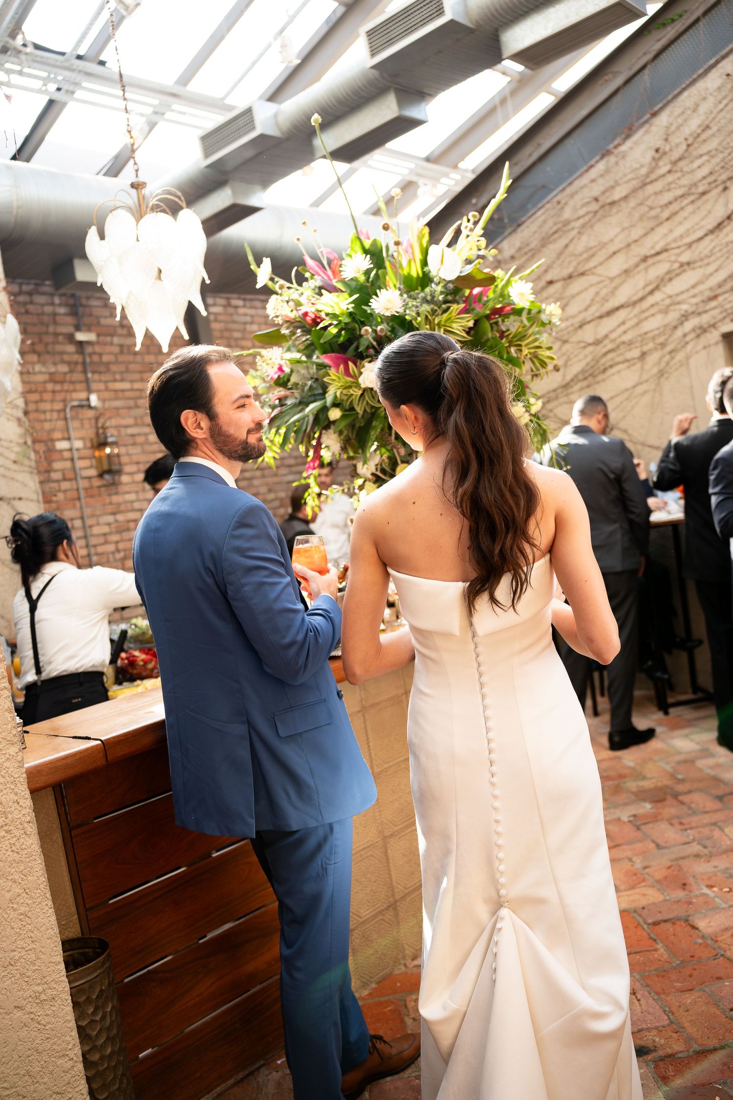 Bride in white gown and groom in blue suit share a moment at their elegant indoor wedding reception.