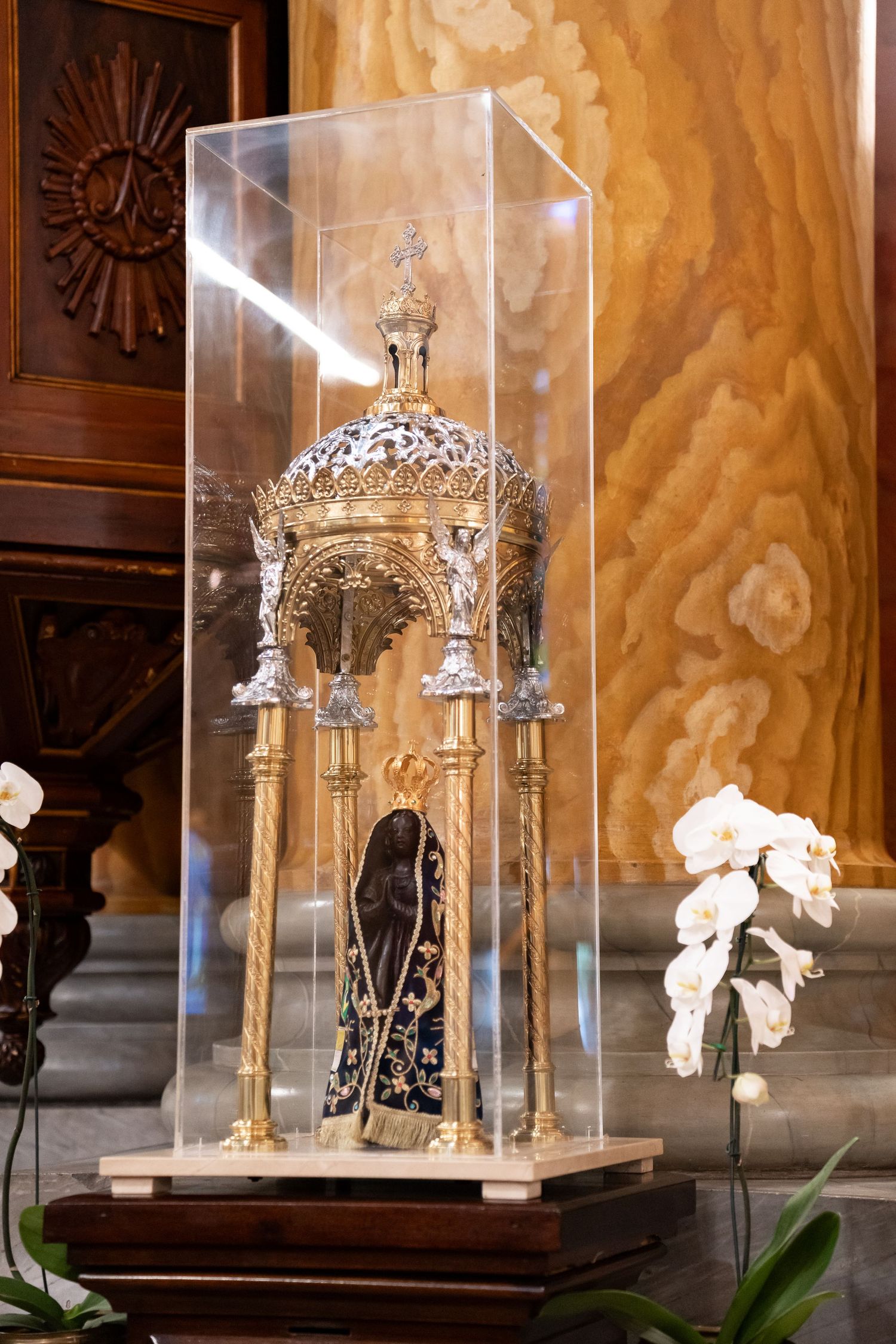 Ornate golden religious reliquary with black Madonna figurine displayed under a glass case in a church.