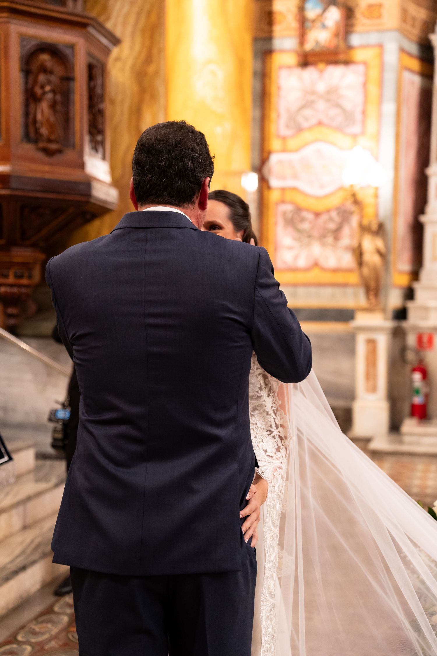Bride and groom embracing at the altar during a church wedding ceremony, bride wearing lace gown and veil.