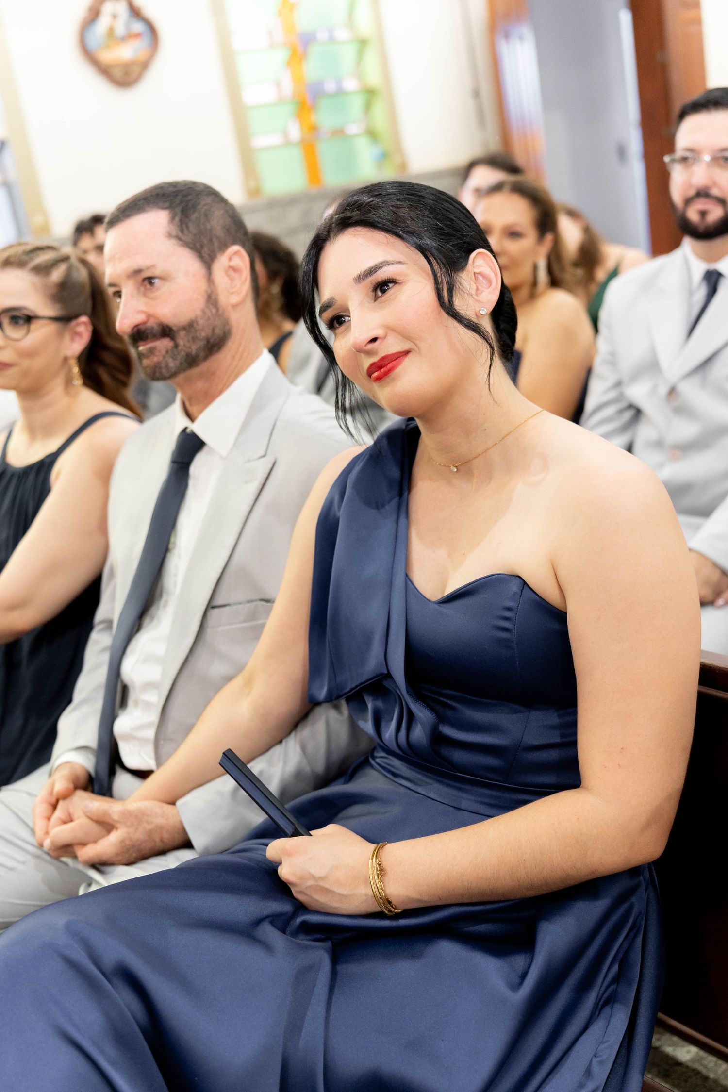 Woman in navy blue gown seated at a formal event, with guests in elegant attire visible in the background.