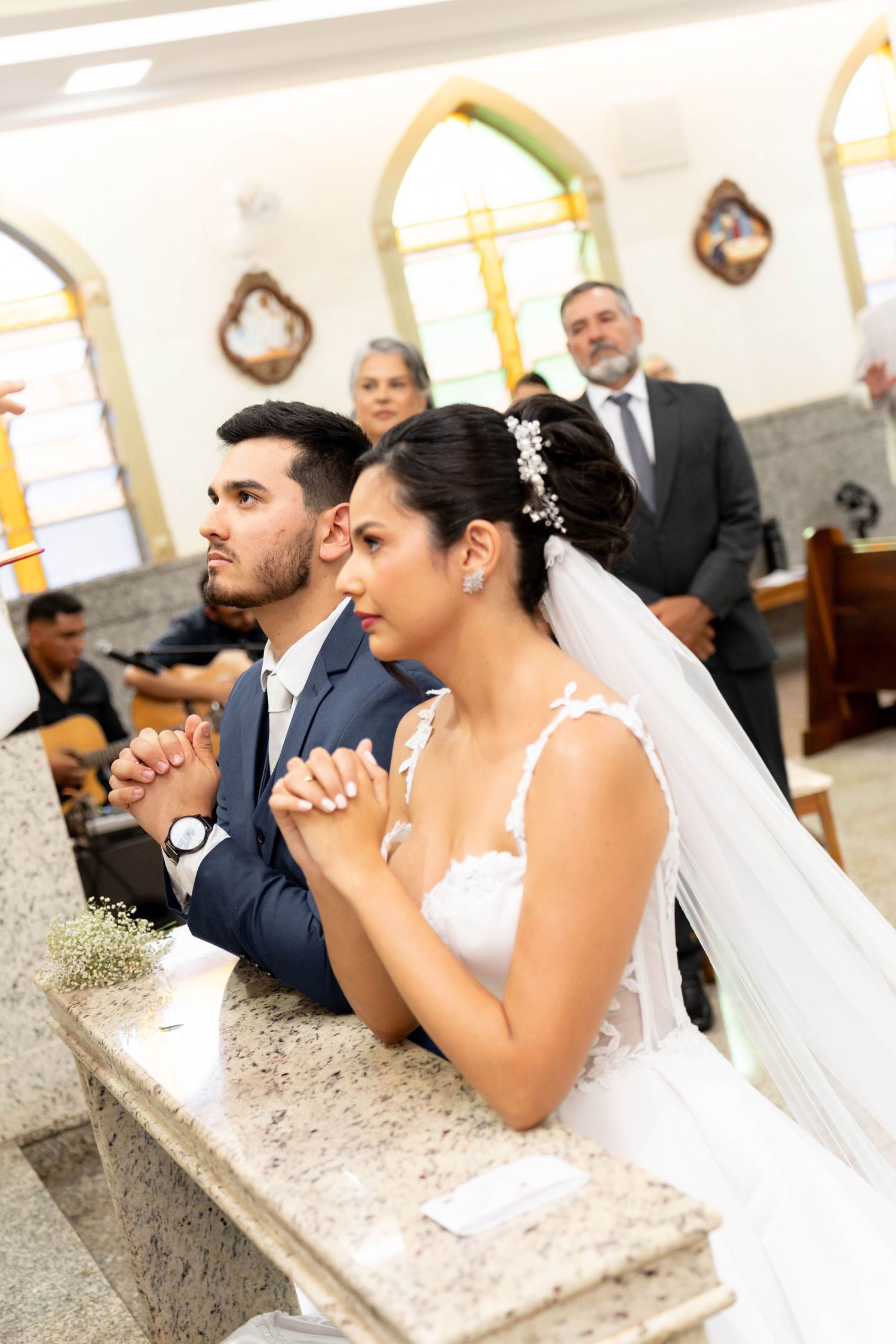 Bride and groom kneeling in prayer at church altar during Catholic wedding ceremony.