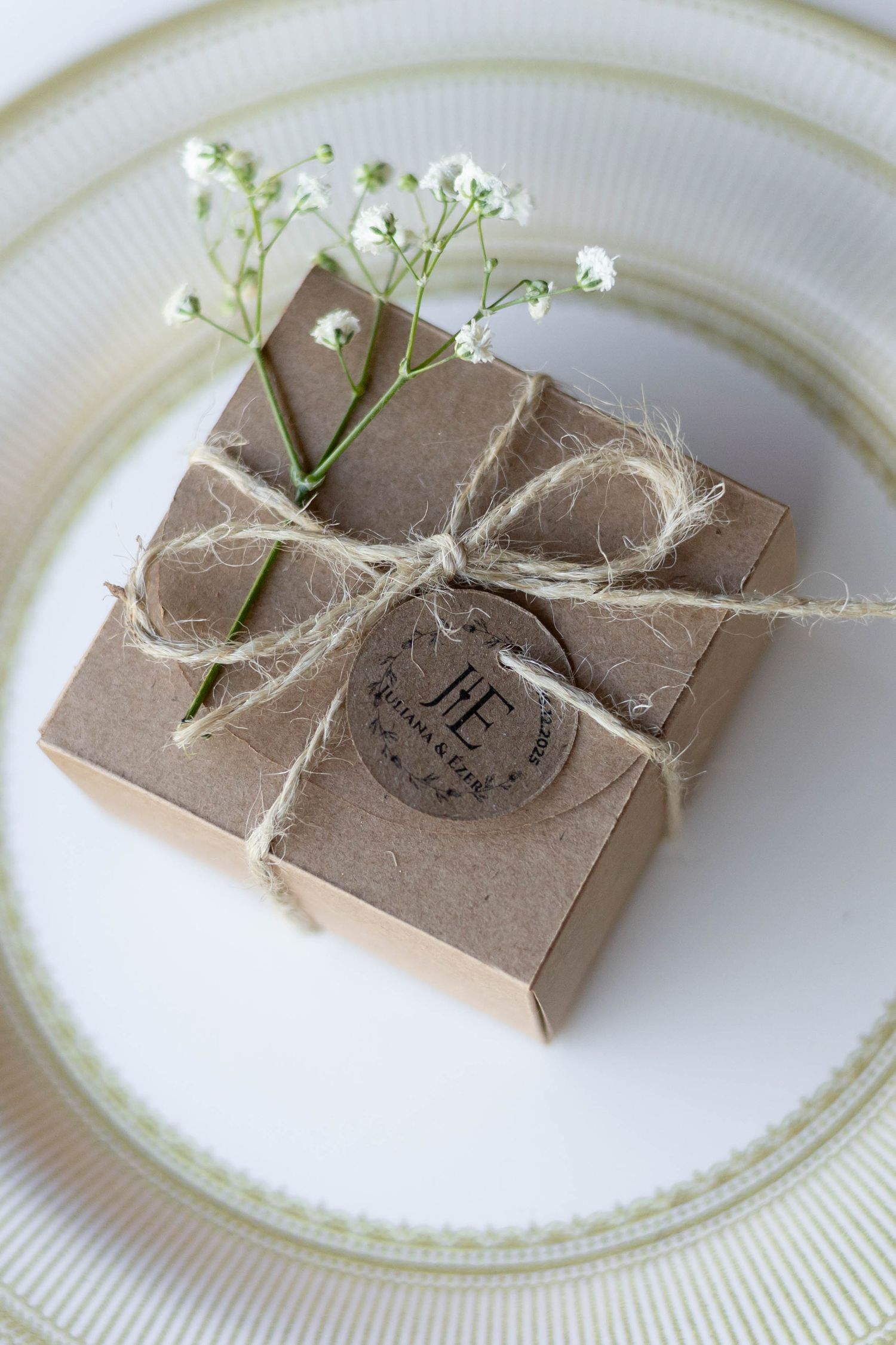 Rustic kraft paper gift box tied with twine bow and baby's breath flowers on a white plate.